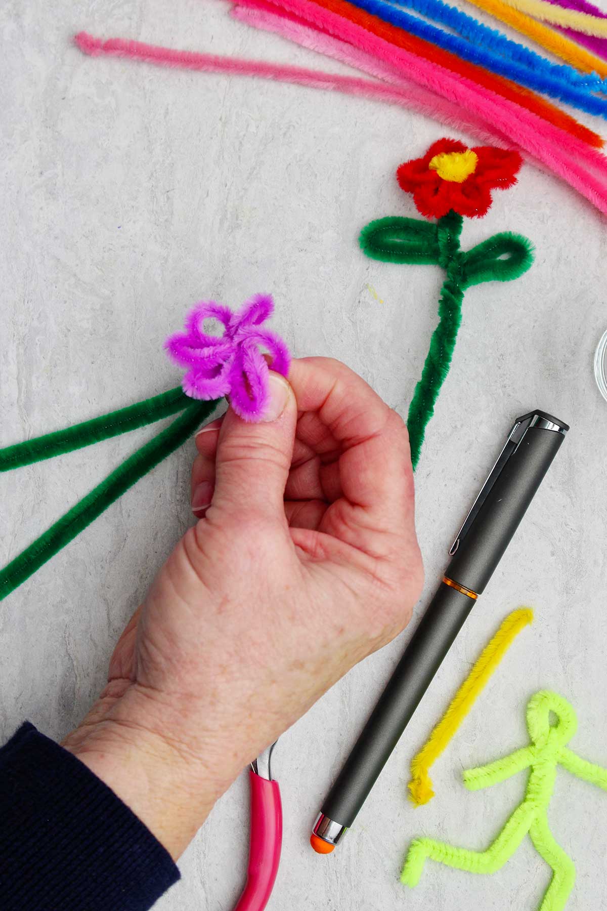 Person holding the pipe cleaner flower while creating the purple pedals.