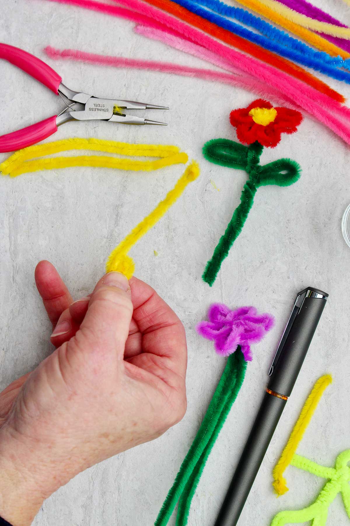 A person holding a yellow pipe cleaner to make the center of the flower.