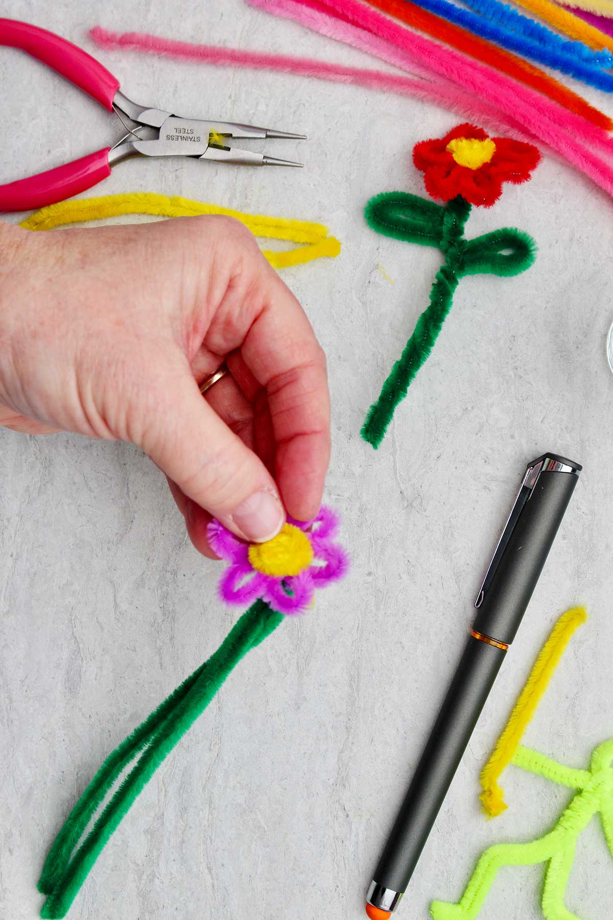 A person attaching the yellow pipe cleaner to the center of the purple flower.