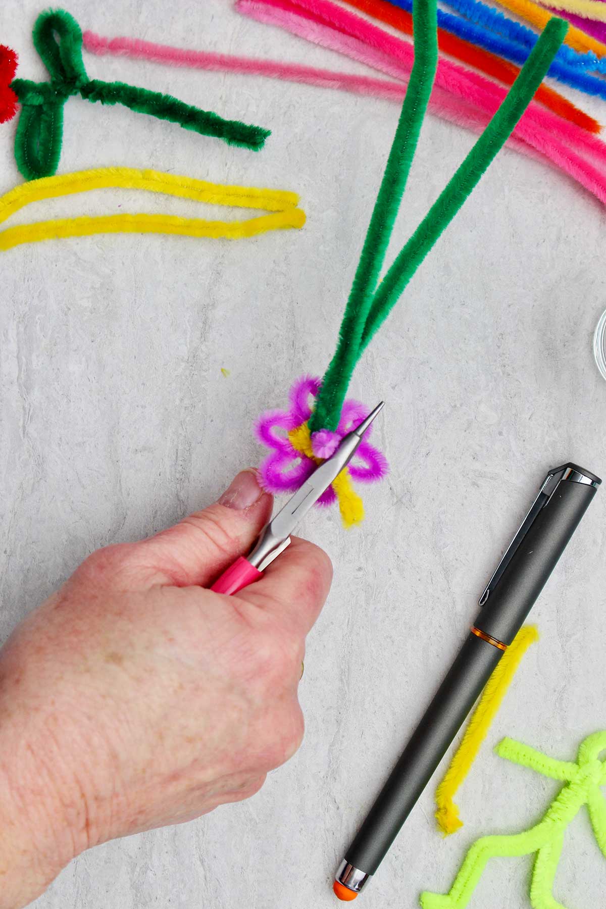 A person bending and trimming the excess yellow pipe cleaner on the back of the flower.