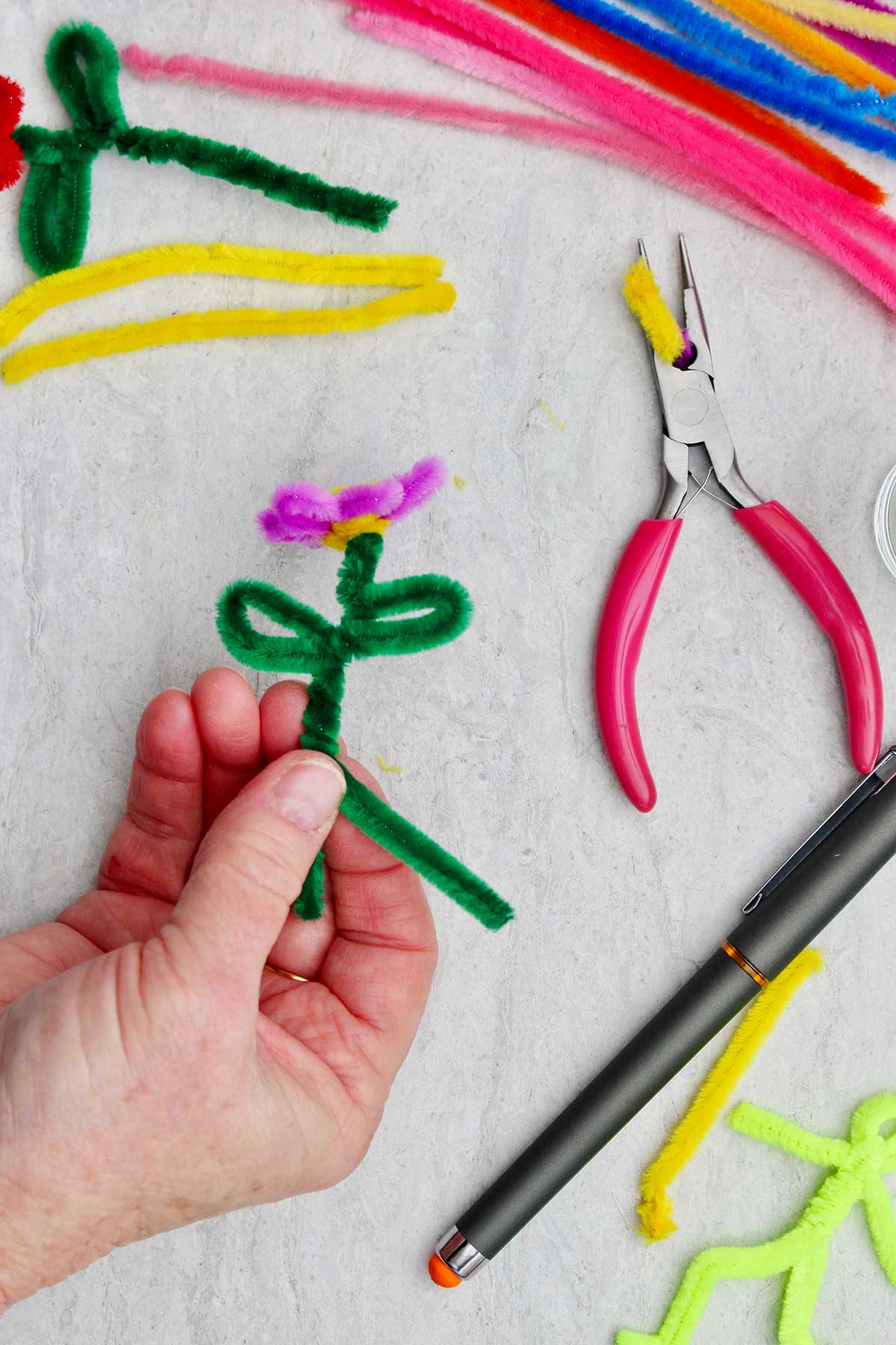 A person twisting the two green pipe cleaners to make a stem for the purple flower.
