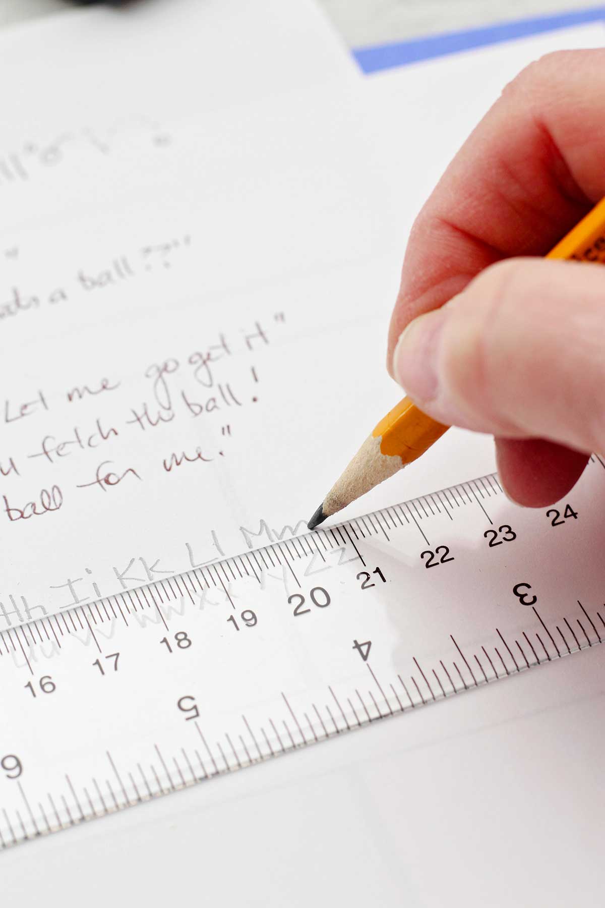 A person measuring and writing out the alphabet in pencil.