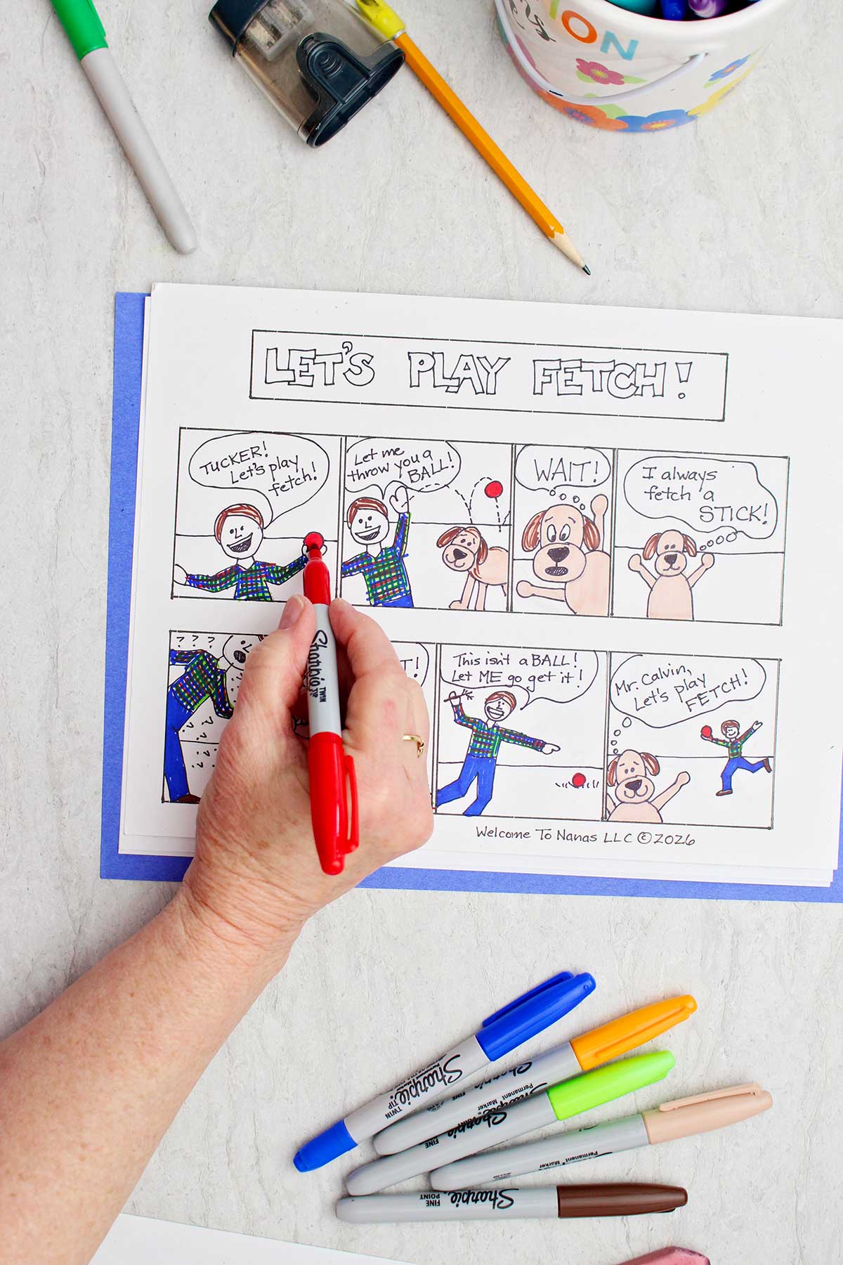 A person coloring a ball on a comic strip about a boy and his dog red.