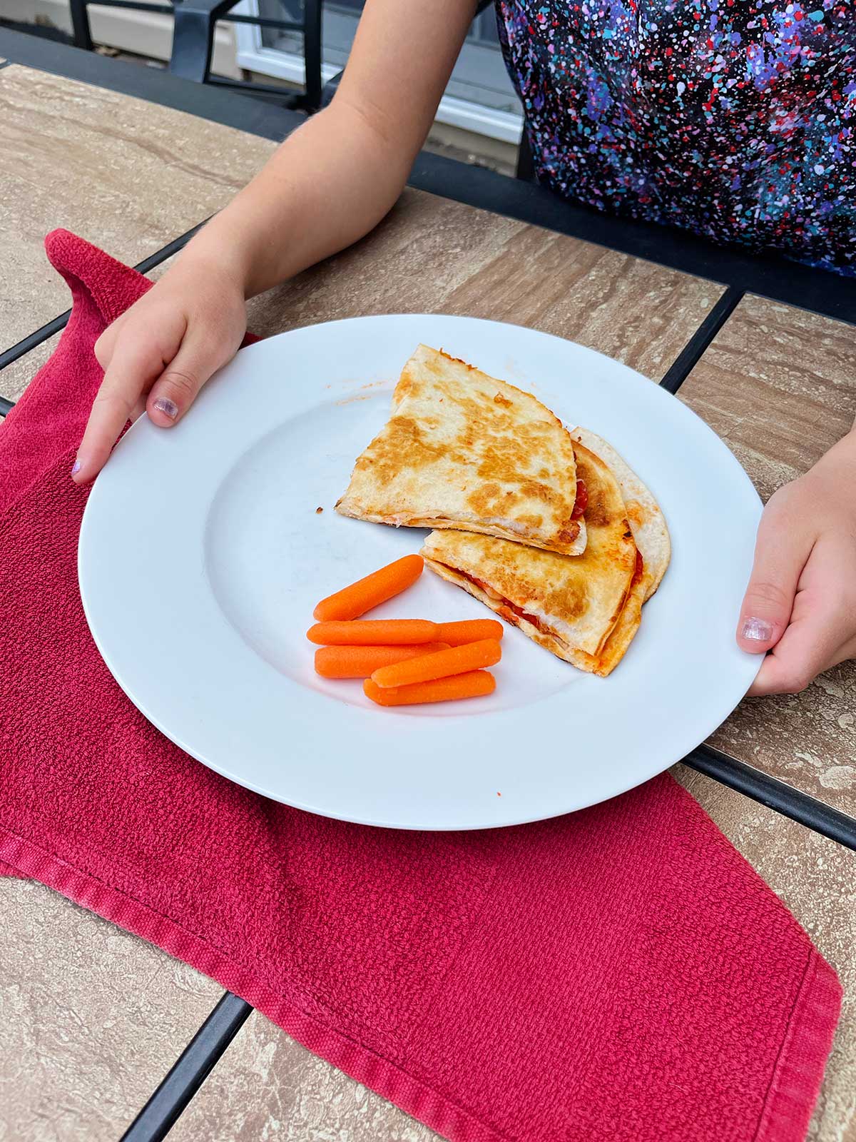 Two pizza quesadillas and baby carrots on a white plate.