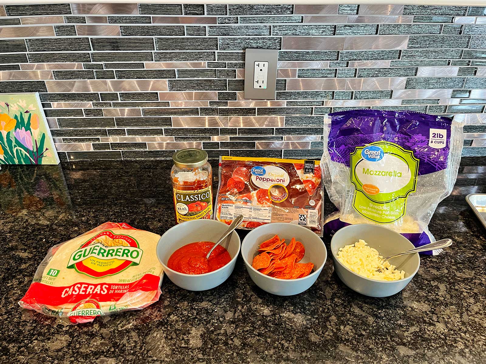 Supplies to make a pizza quesadilla sitting on a dark marble countertop.