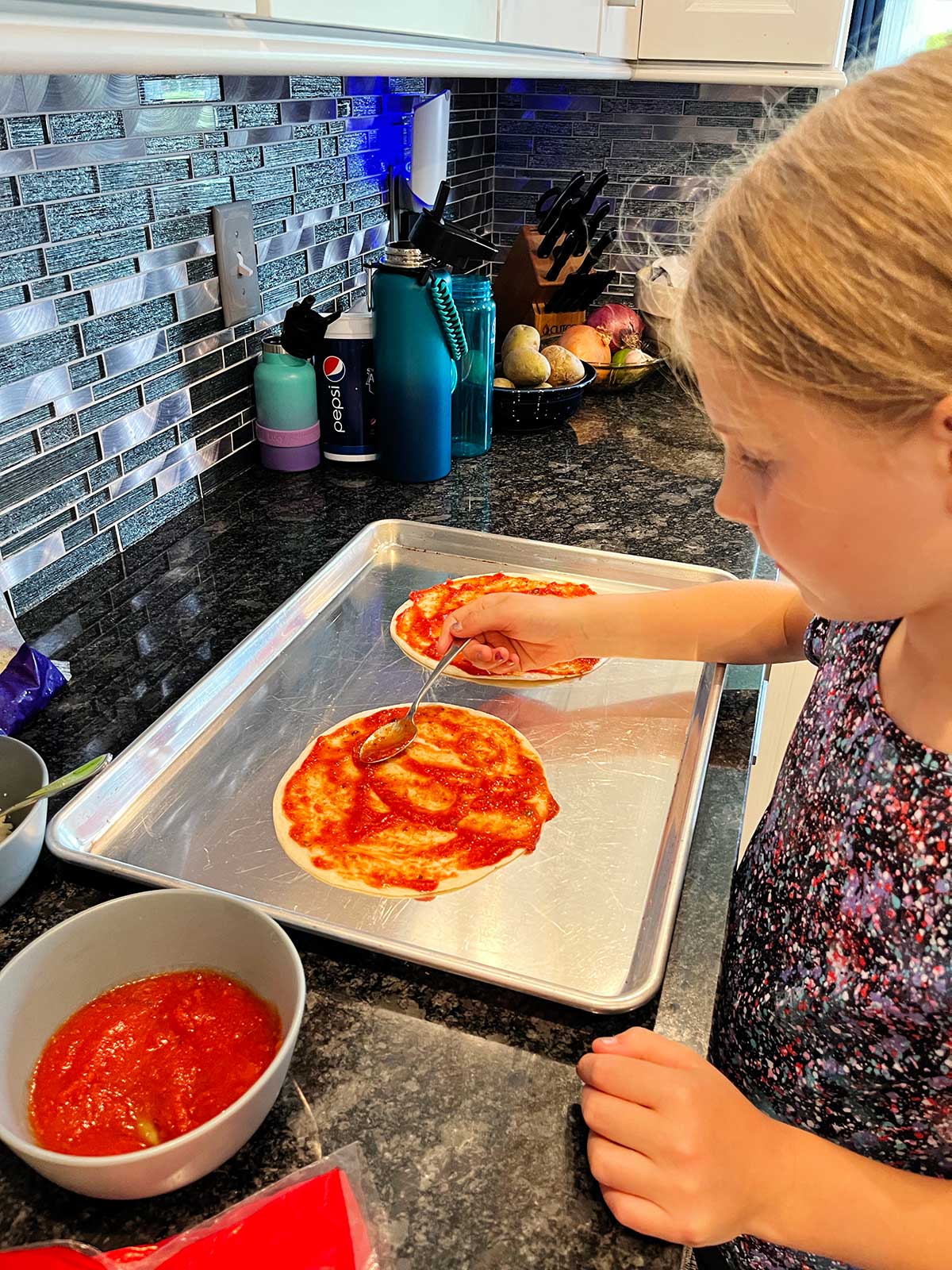 A child placing sauce on the pizza quesadilla.