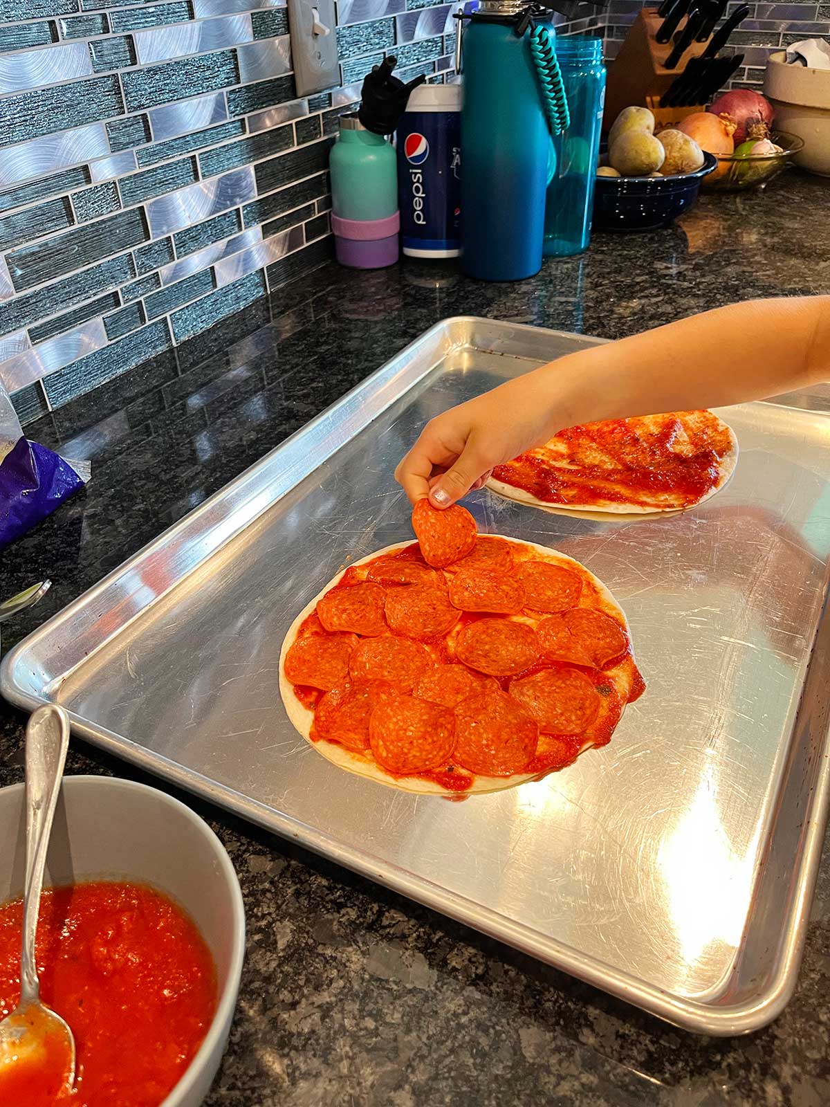 A child placing pepperoni on the pizza quesadilla.
