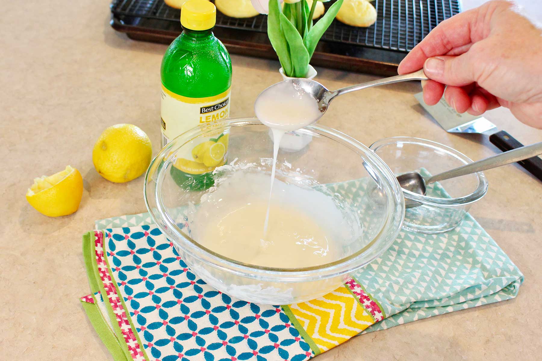 A person mixing up some lemon glaze in a bowl on a colorful hand towel on a counter top.
