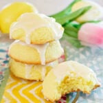 Three lemon cake cookies stacked on a colorful placemat and one cookie with a bite missing.