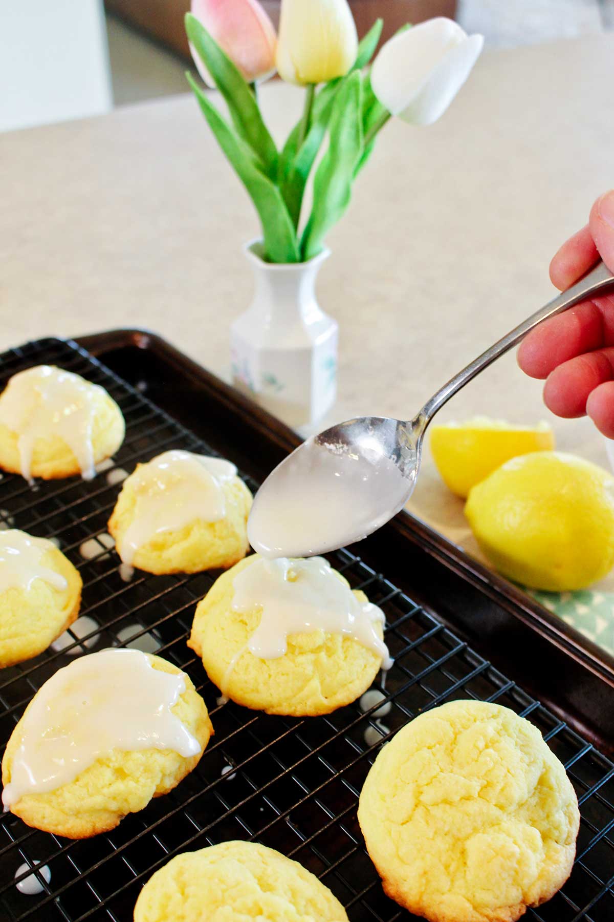 A person glazing lemon cake cookies on a cooling rack.