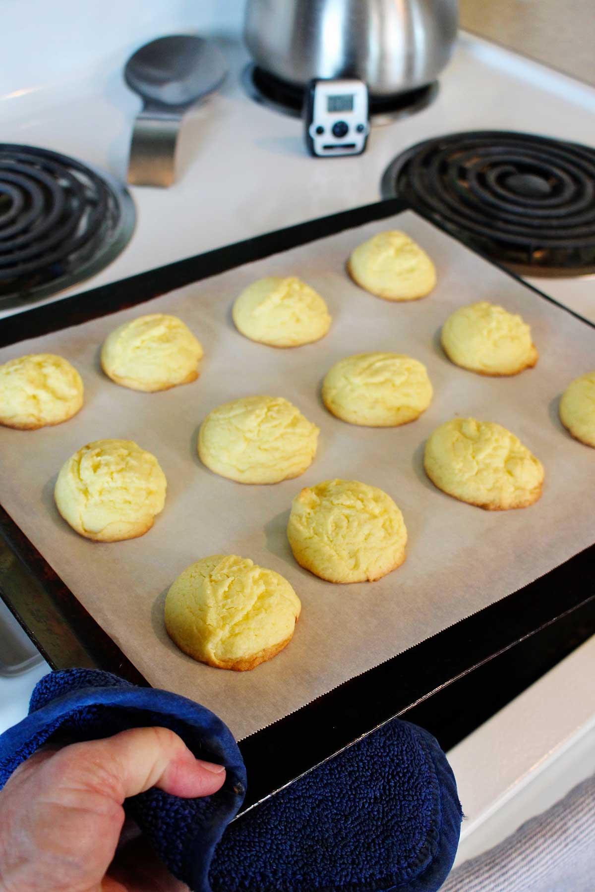 A person taking a baking sheet of baked lemon cake cookies out of the oven.