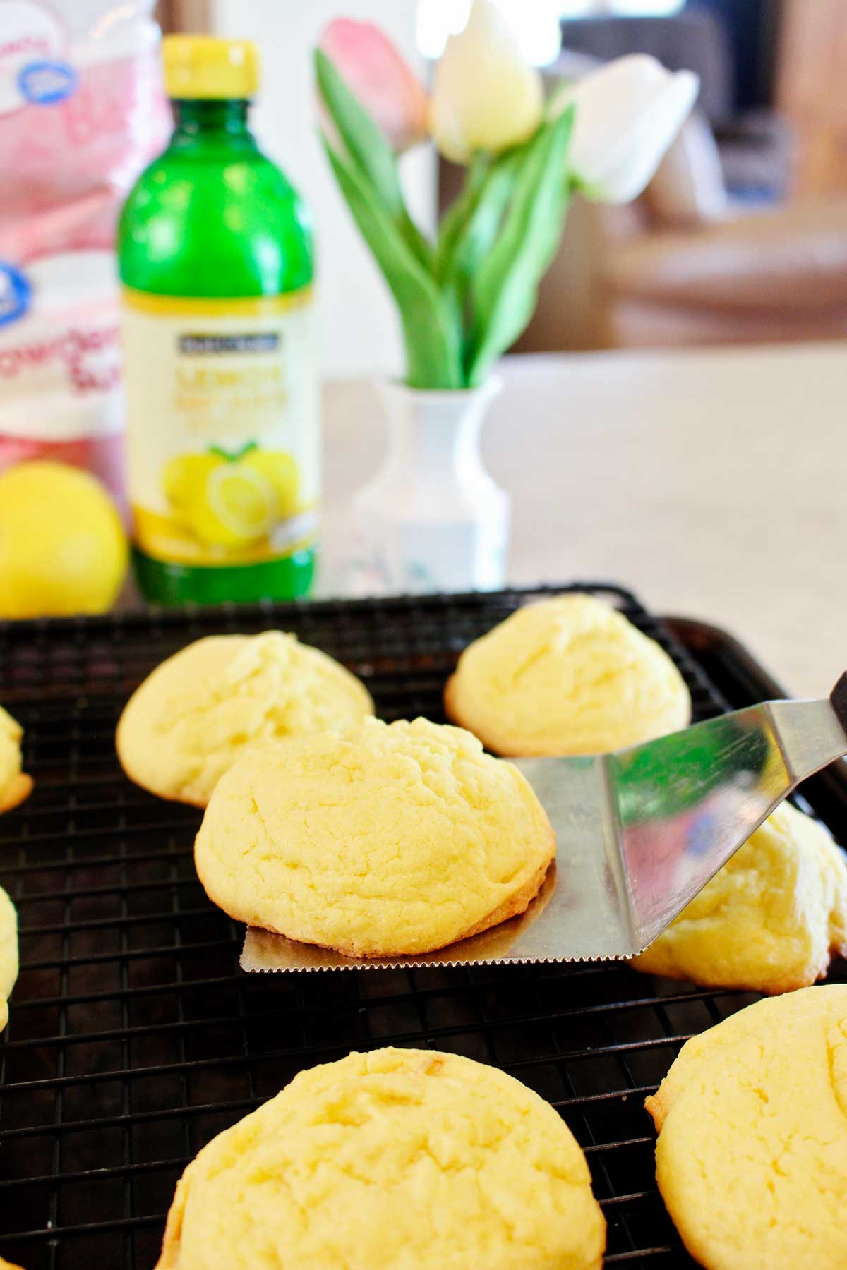 A person lifting a freshly baked cookie and placing it on a cooling rack.