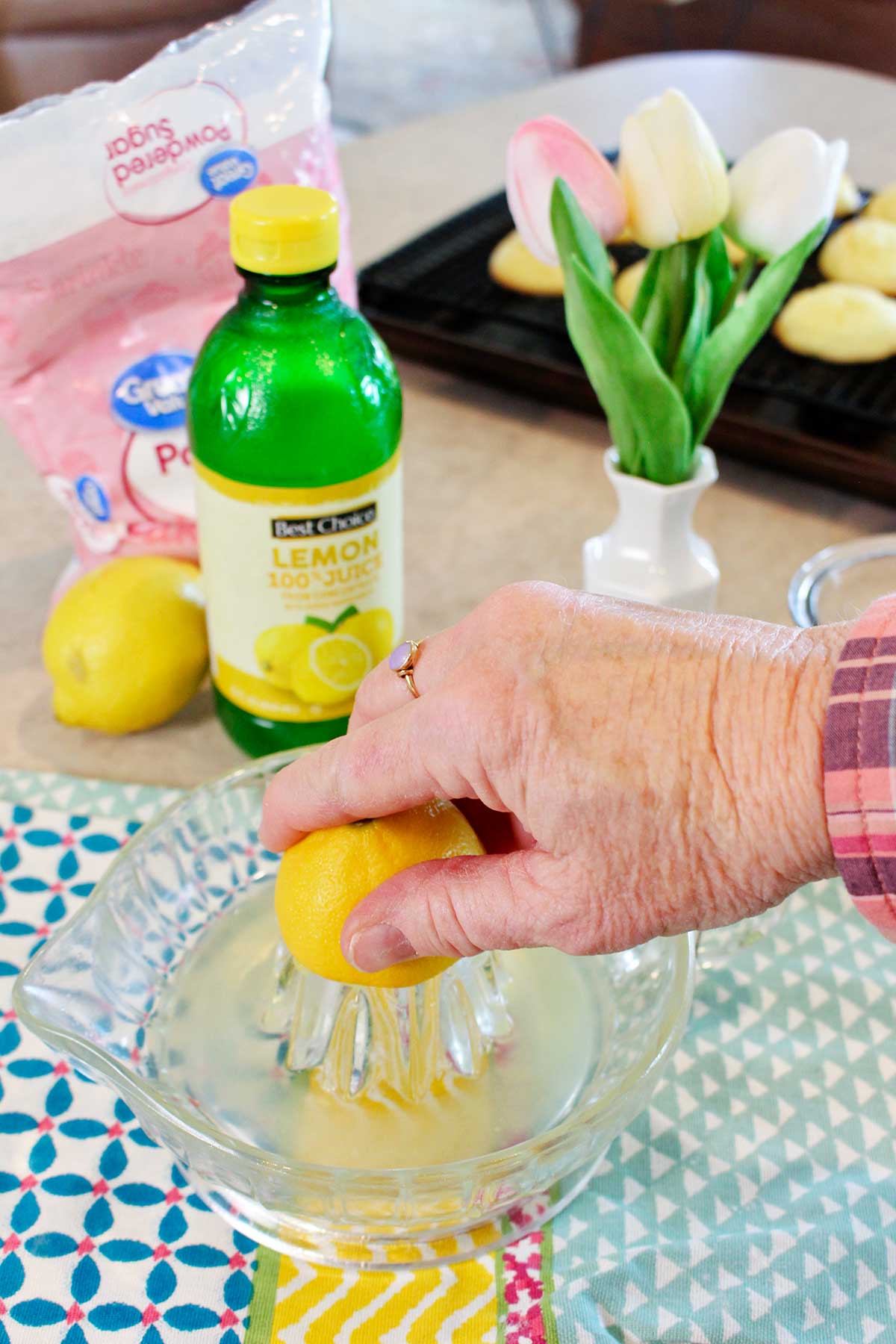 A person juicing a lemon on a colorful hand towel with cookies and flowers in the background.
