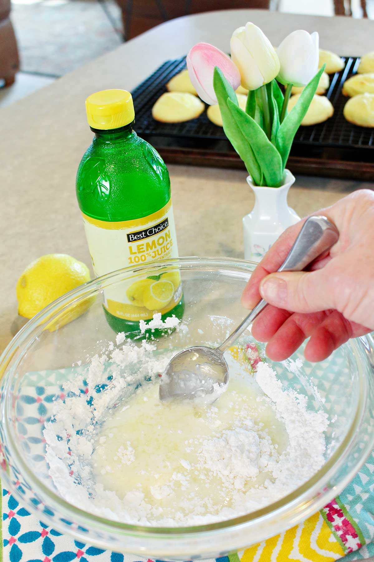 A person mixing up some lemon glaze in a bowl on a colorful hand towel on a counter top.