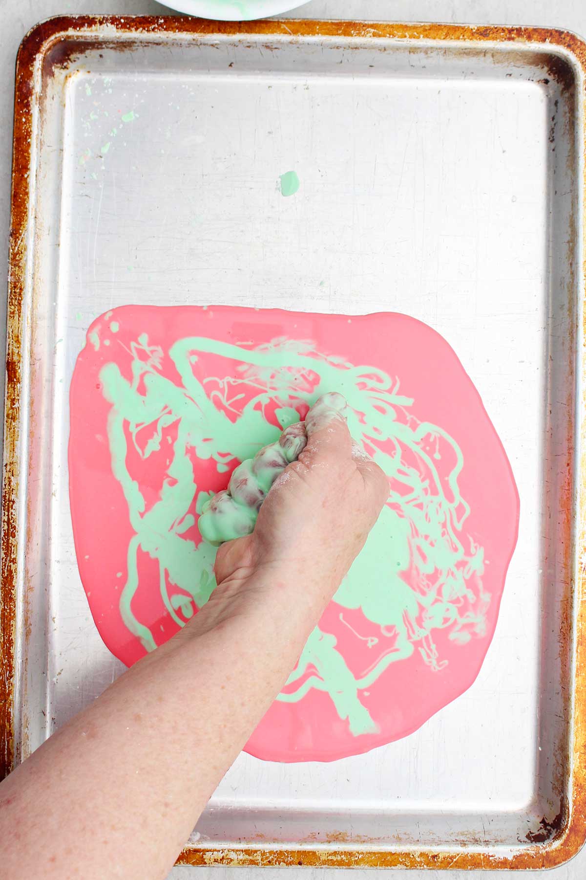 A person squeezing a handful of oobleck over a cookie sheet.