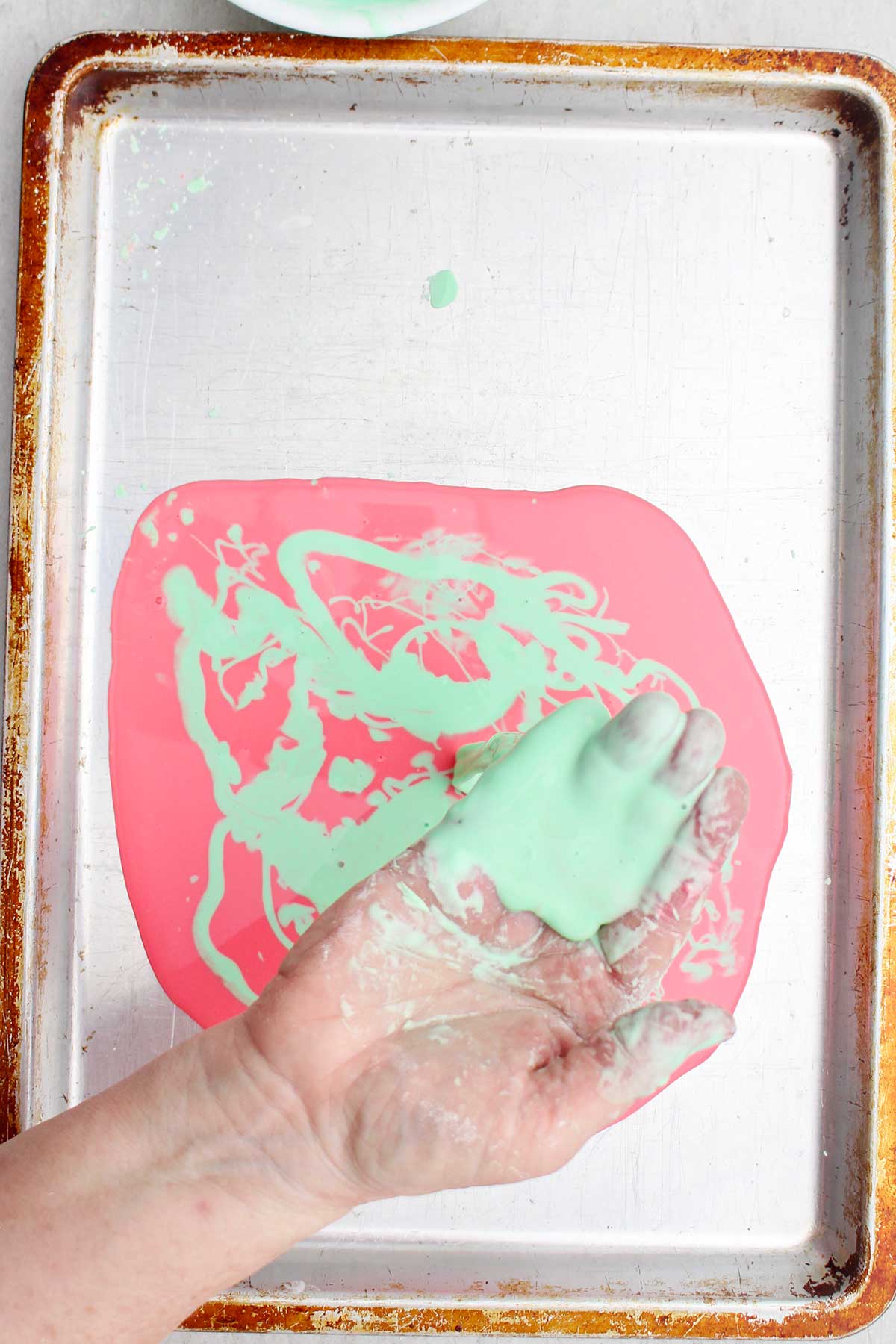 A person holding a handful of light green oobleck over a cookie sheet.