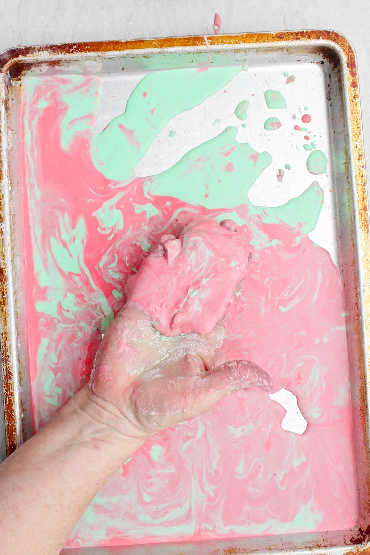 A person playing with a more liquid state of the oobleck on a cookie sheet.