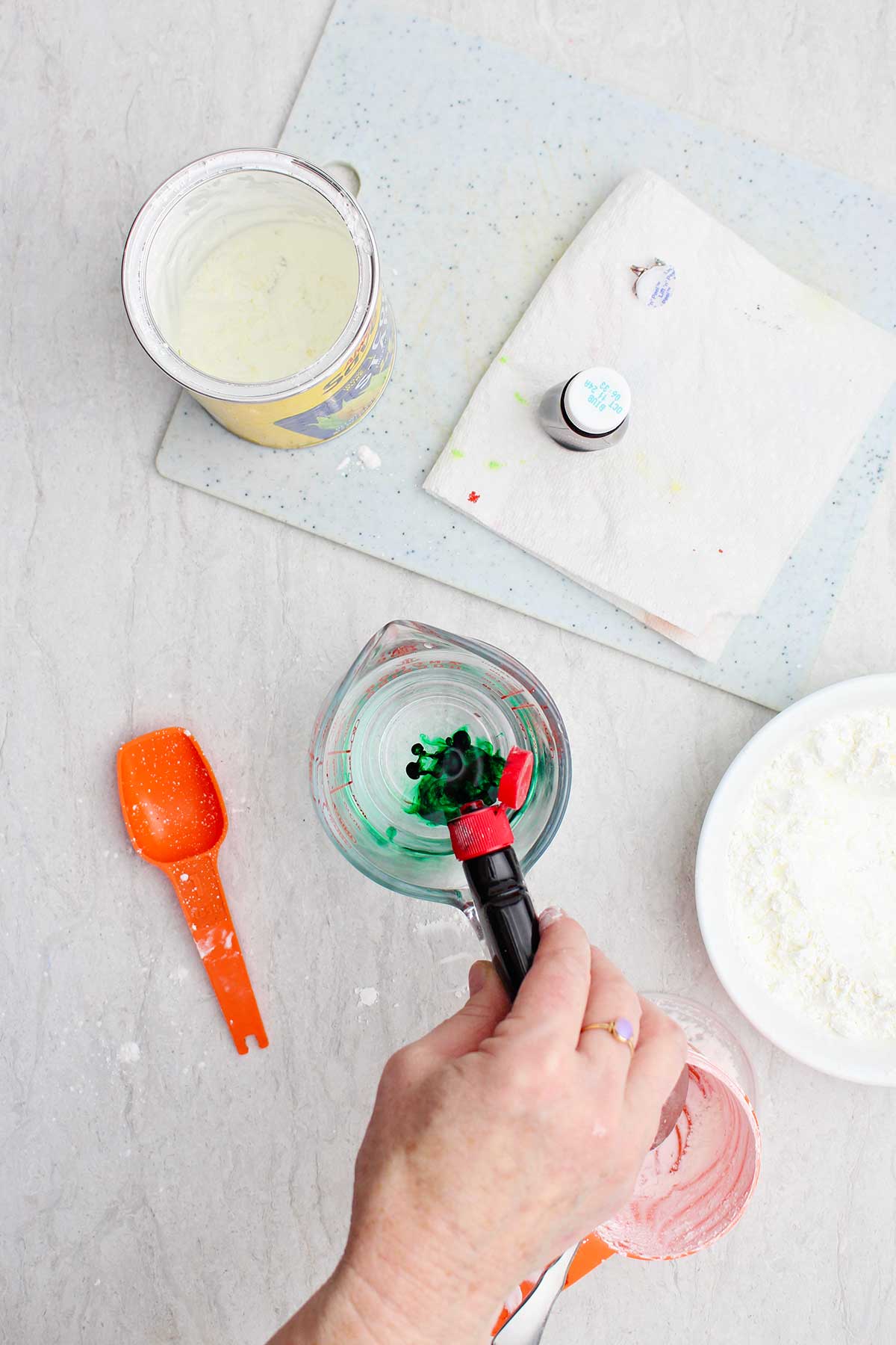 A person squeezing green food coloring into a measuring cup of water.