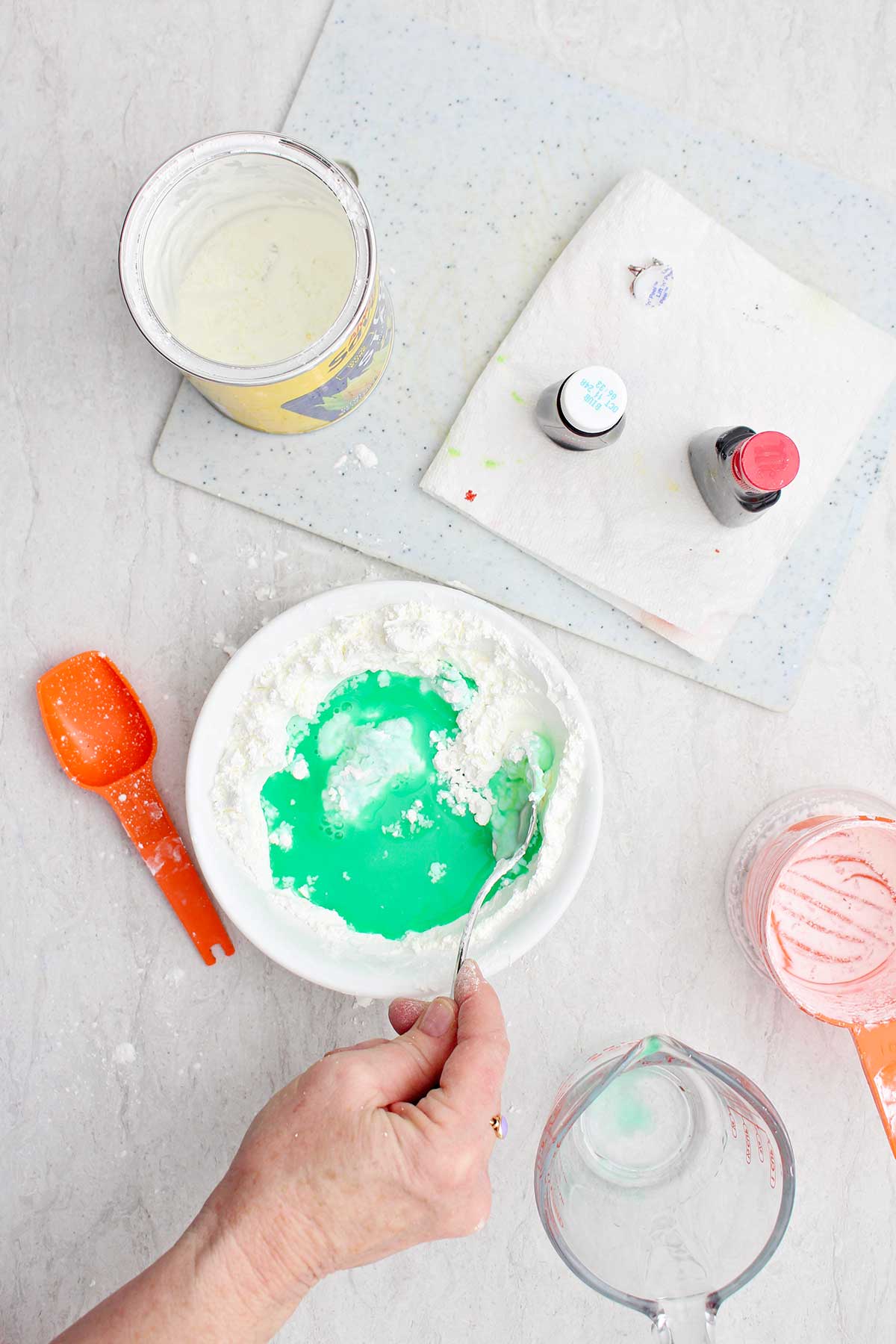 A person mixing together cornstarch, water and green food coloring in a white bowl.
