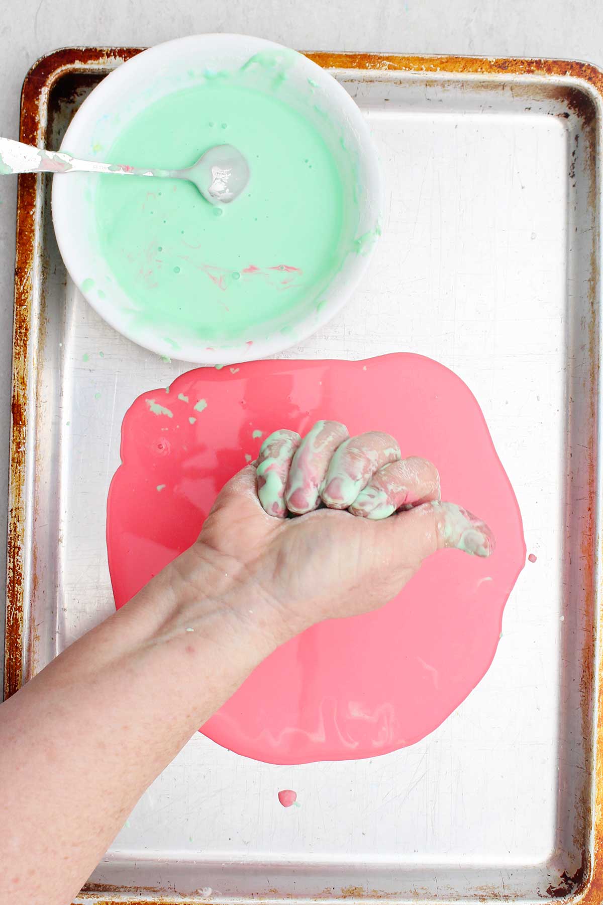 A person squeezing a handful of oobleck over a cookie sheet.