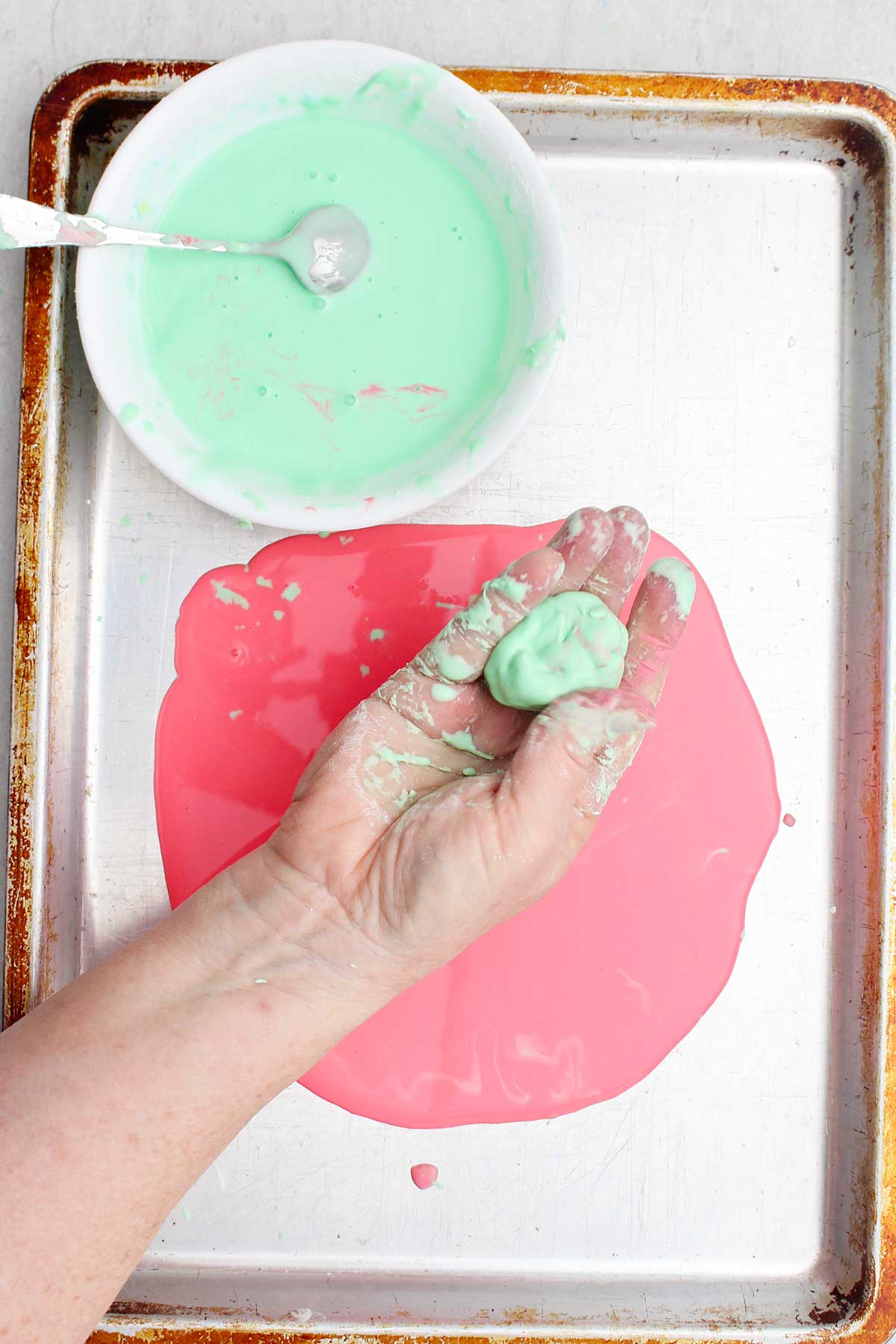 A person showing a ball of light green oobleck over a cookie sheet.