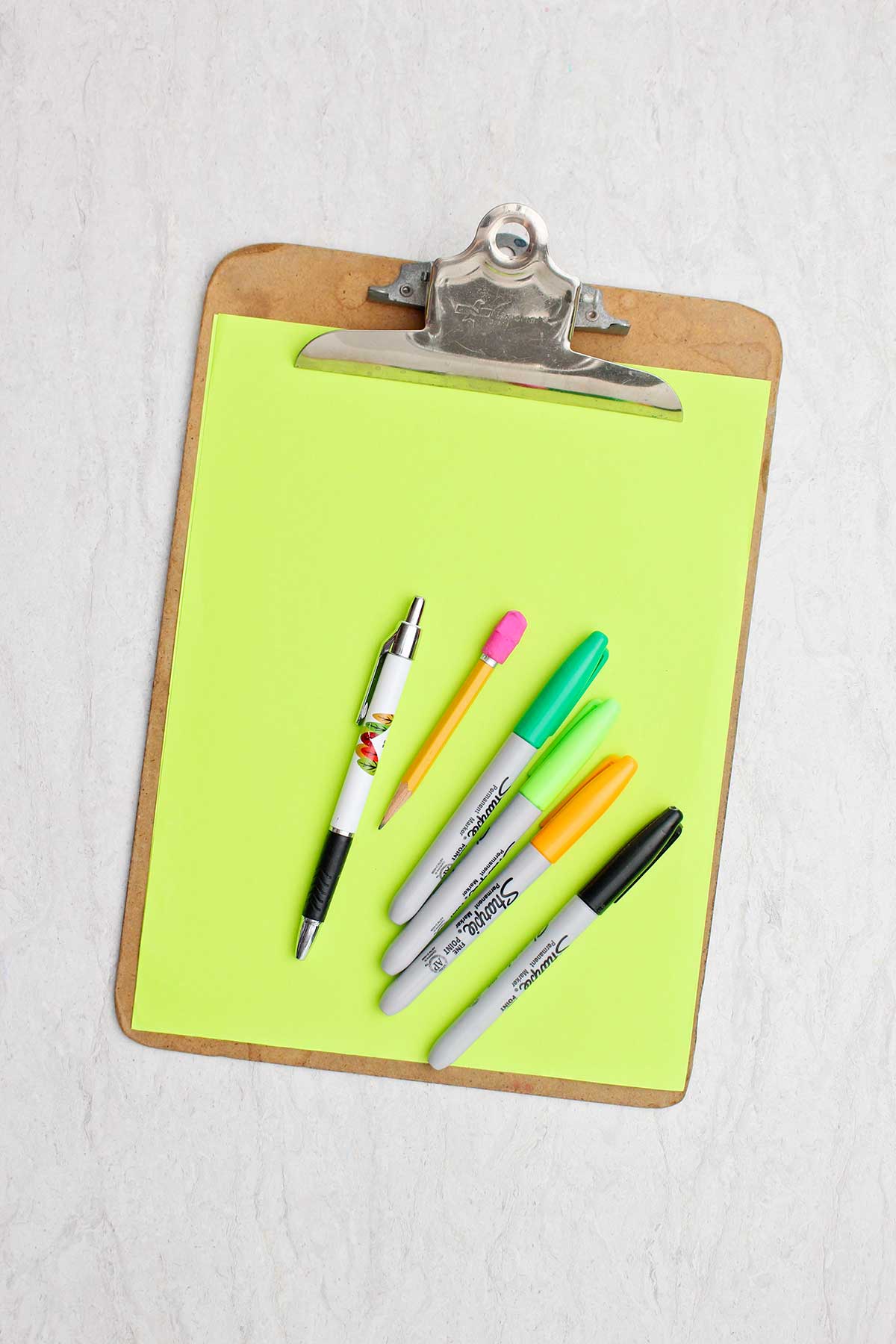 A green piece of paper, pencil, pen and different colored sharpie markers.