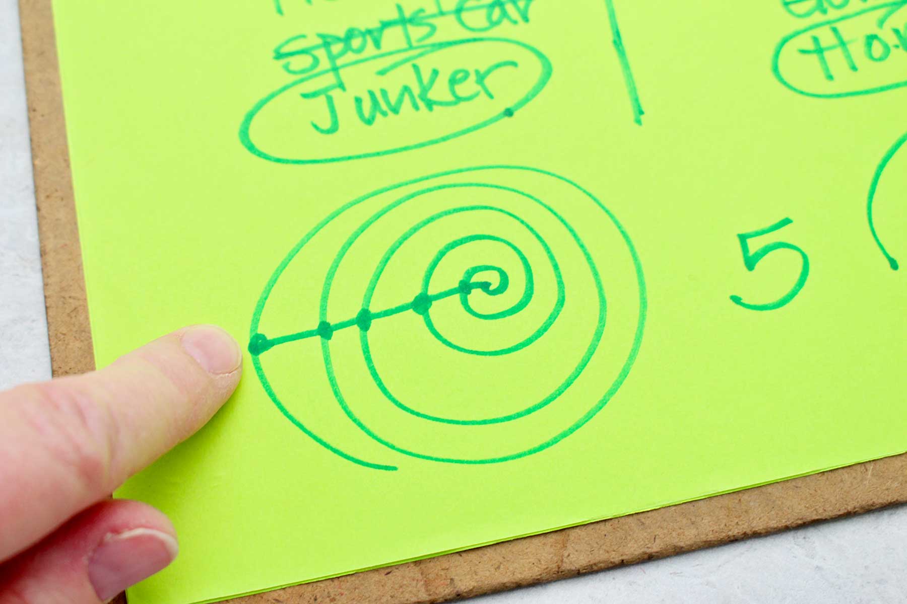 A person showing the swirl and dot drawing that determines how many numbers to count to before crossing an option off on a MASH game.
