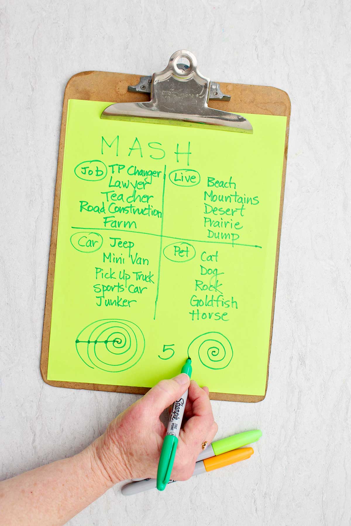A person making a swirl at the bottom of a MASH game with green sharpie.