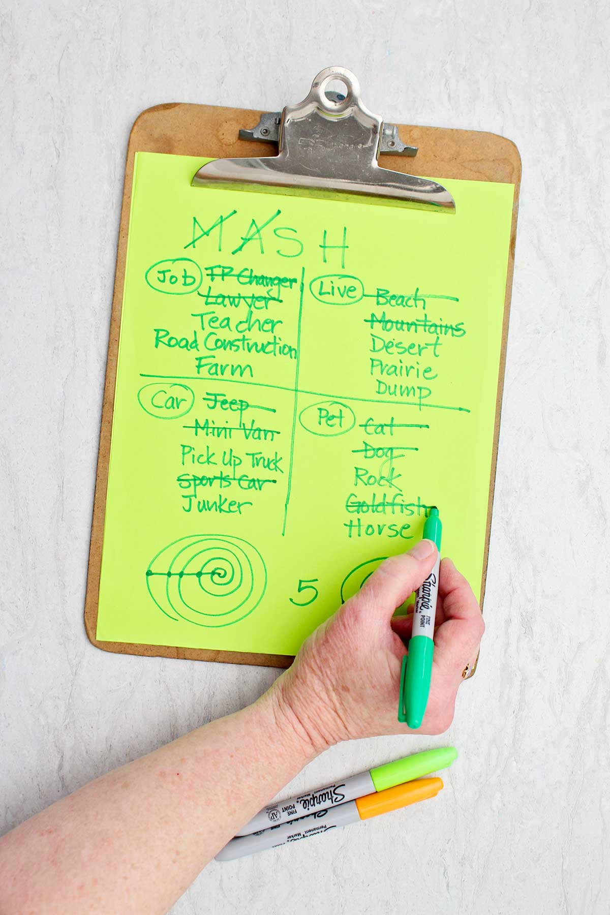 A person crossing off the option of "pet goldfish" with green sharpie on a MASH game.