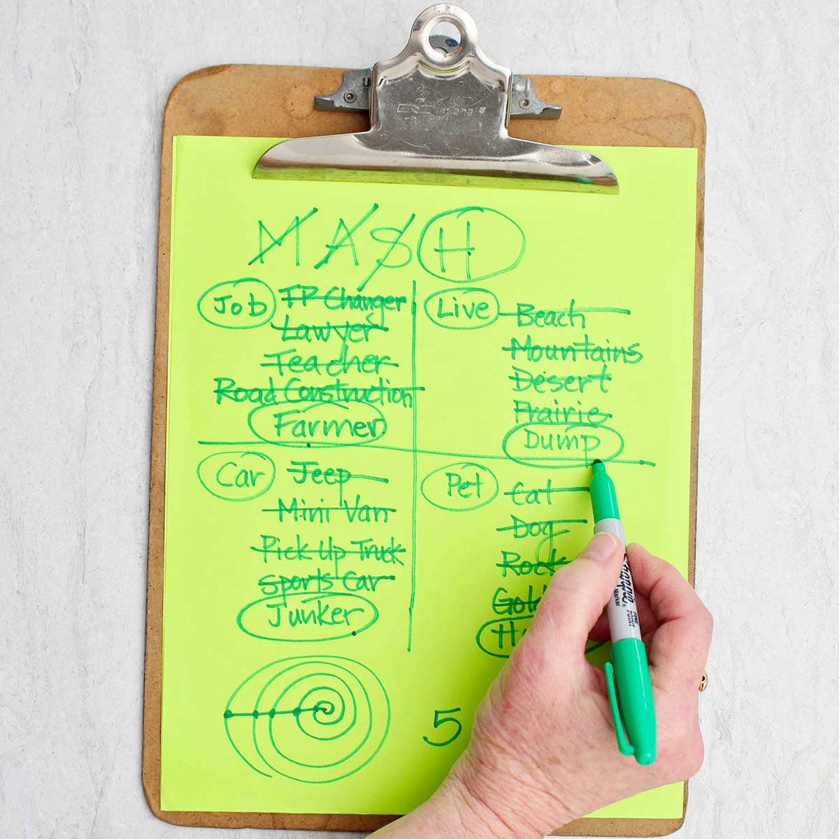 A person circling the living location of "dump" with green sharpie on a MASH game.