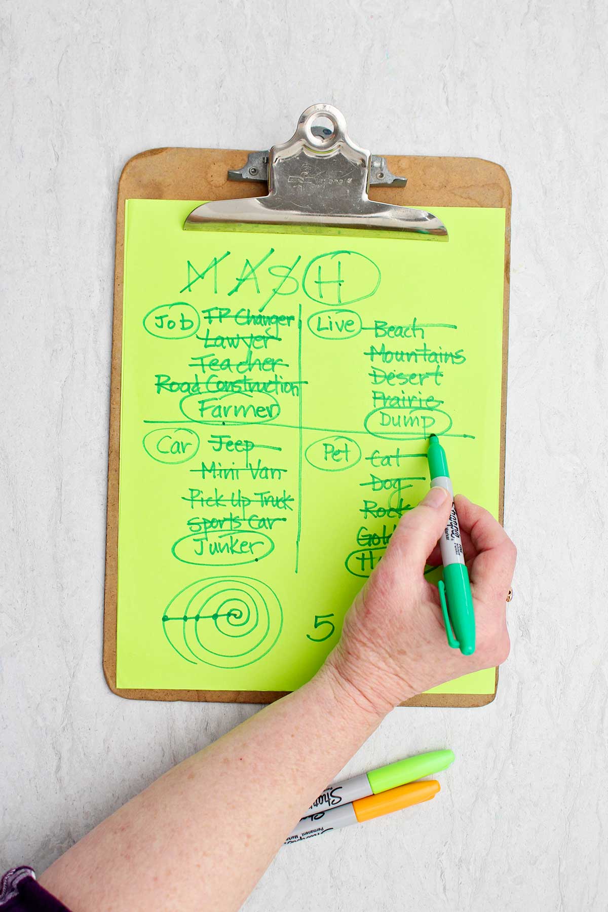 A person circling the living location of "dump" with green sharpie on a MASH game.