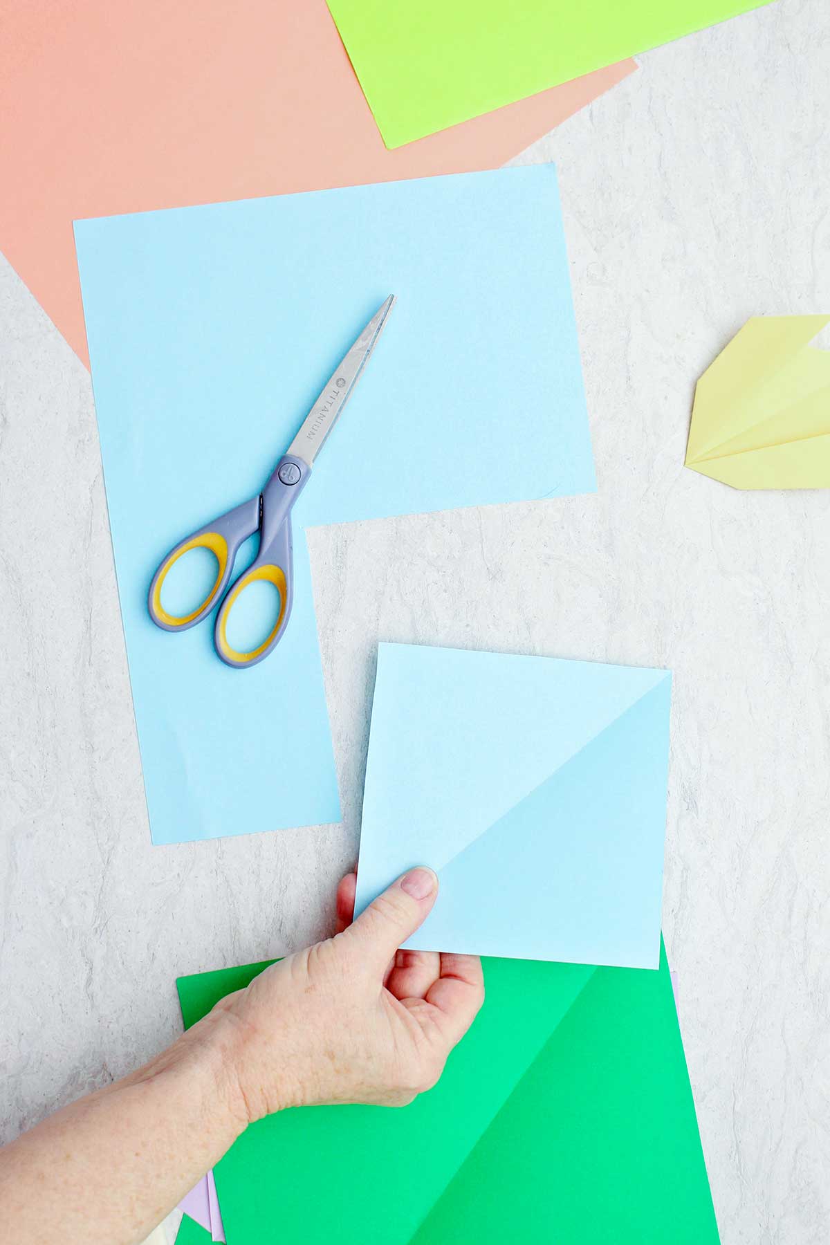 A person cutting out a square of light blue paper to make an origami flower.