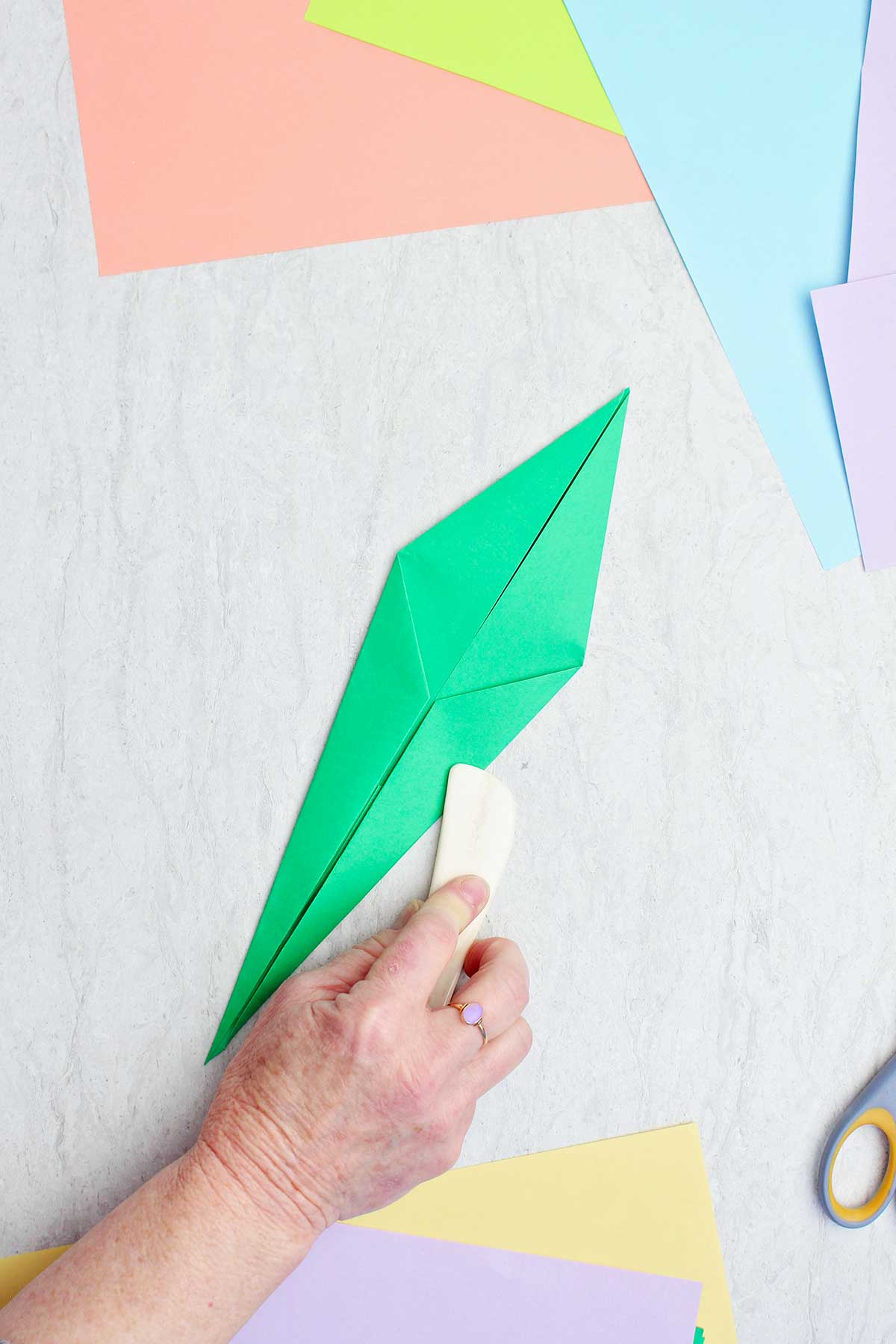 A person using a bone folder to crease a green paper to make a stem.