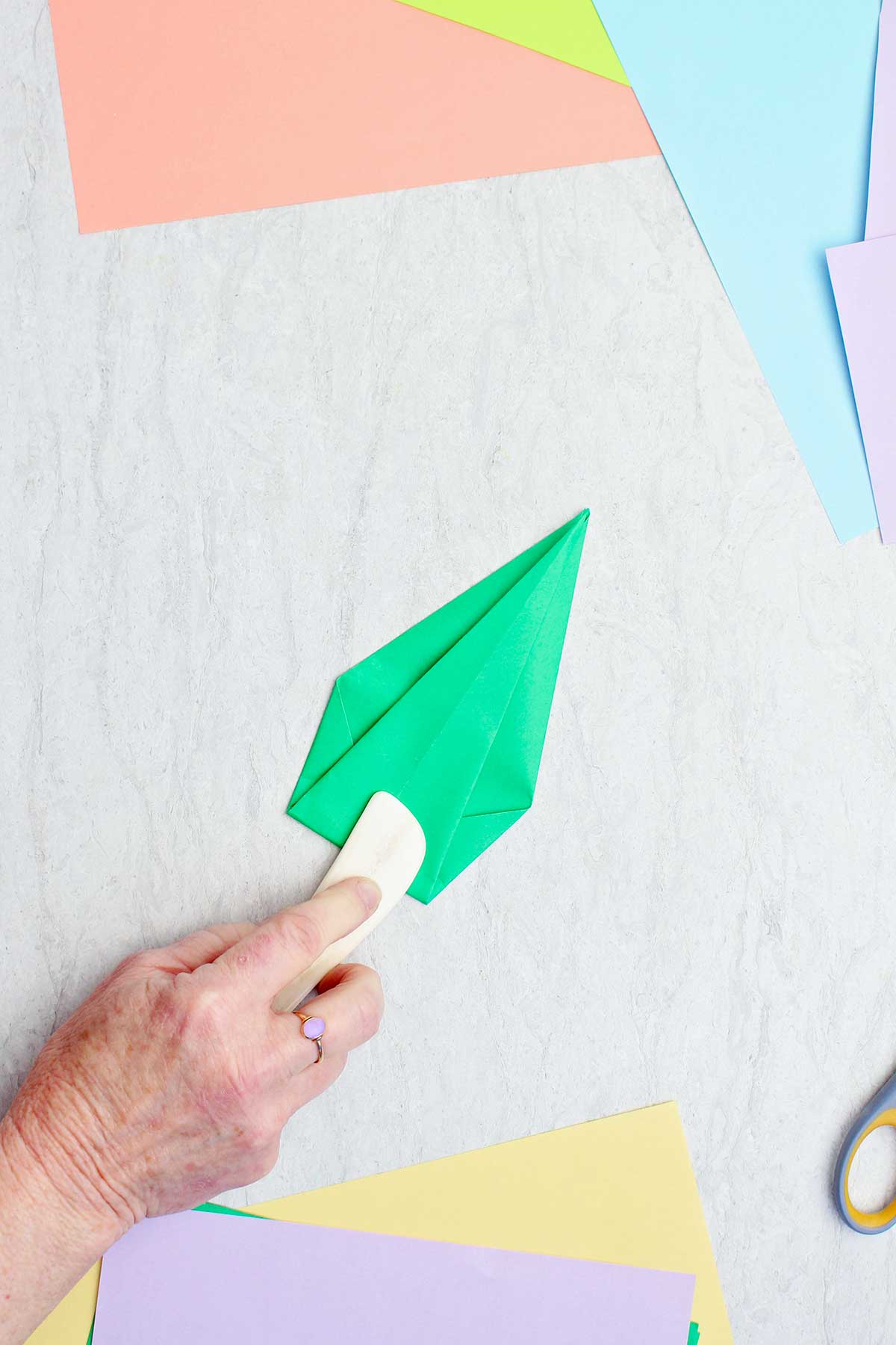A person using a bone folder to crease a green paper to make a stem.