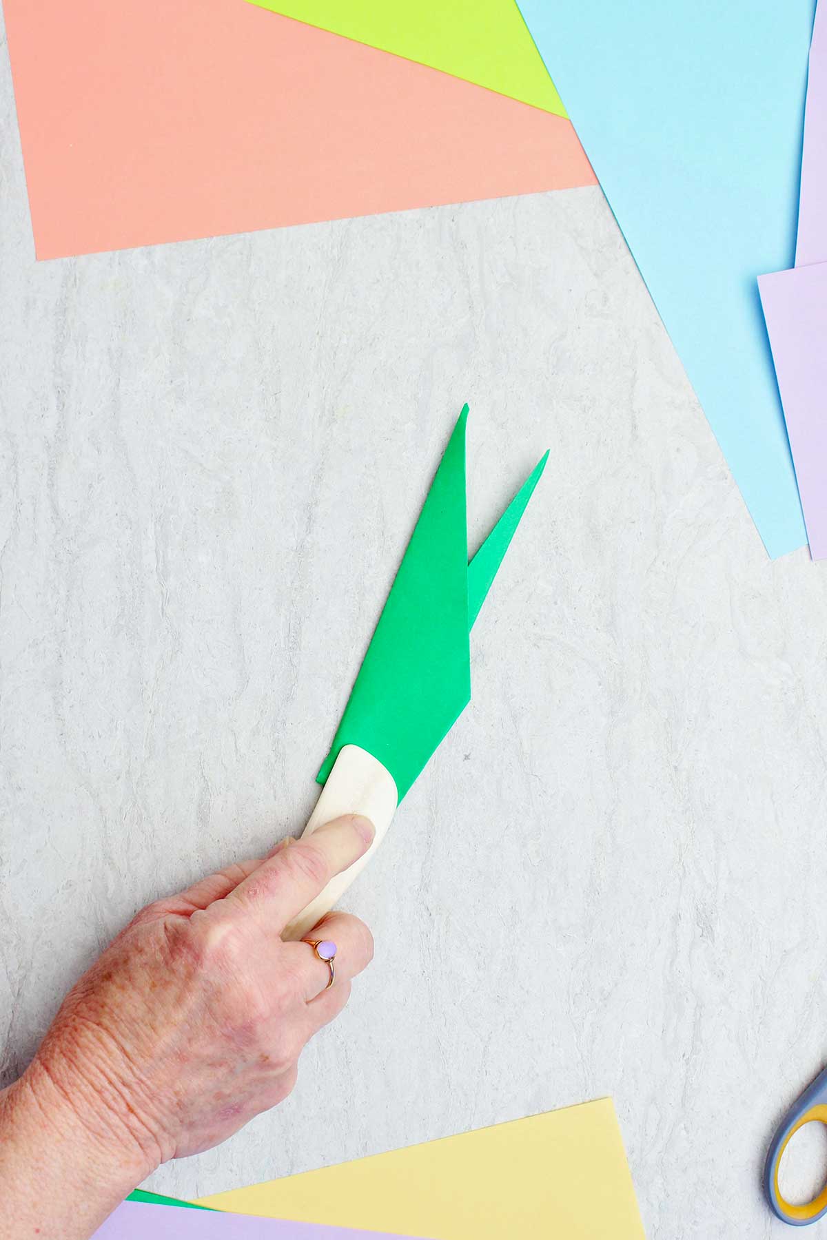 A person using a bone folder to crease a green paper to make a stem.