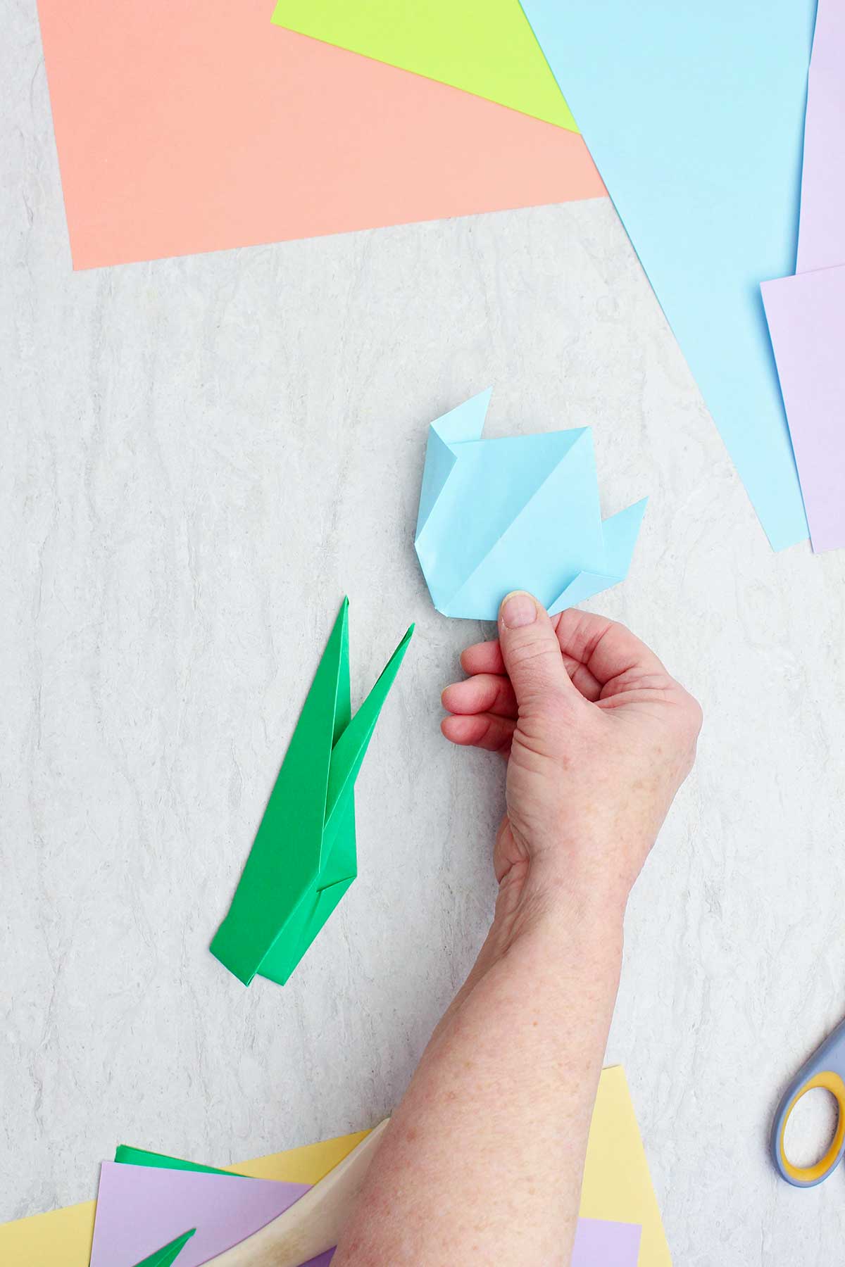 A person placing a light blue origami flower on an origami stem.