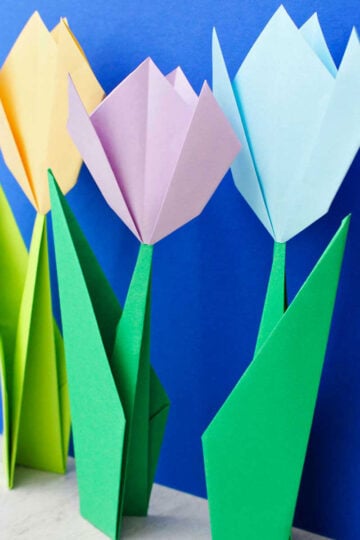 Three origami flowers standing up in front of a bright blue background.