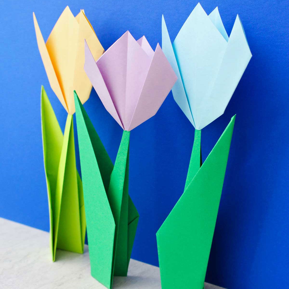 Three origami flowers standing up in front of a bright blue background.