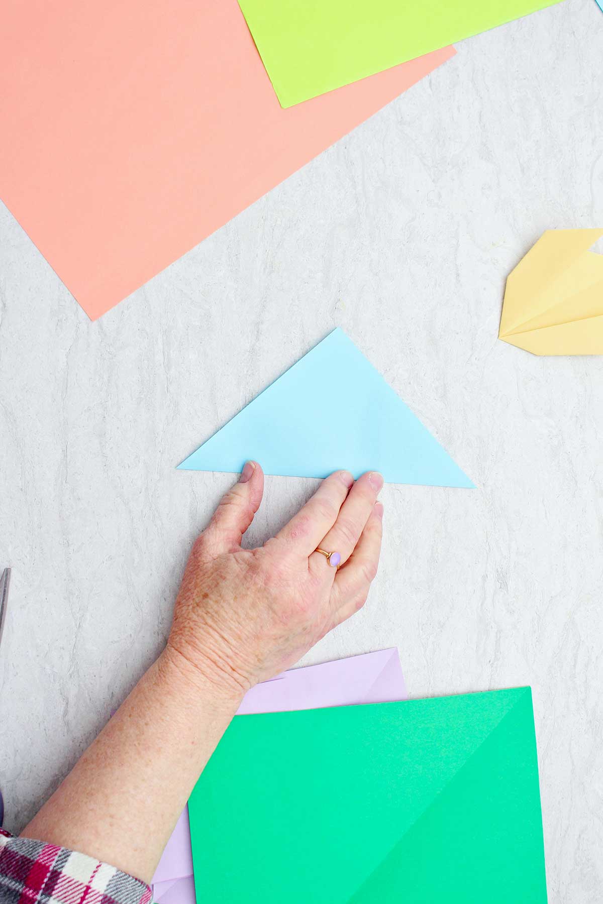 A person folding a light blue piece of paper to make a flower.