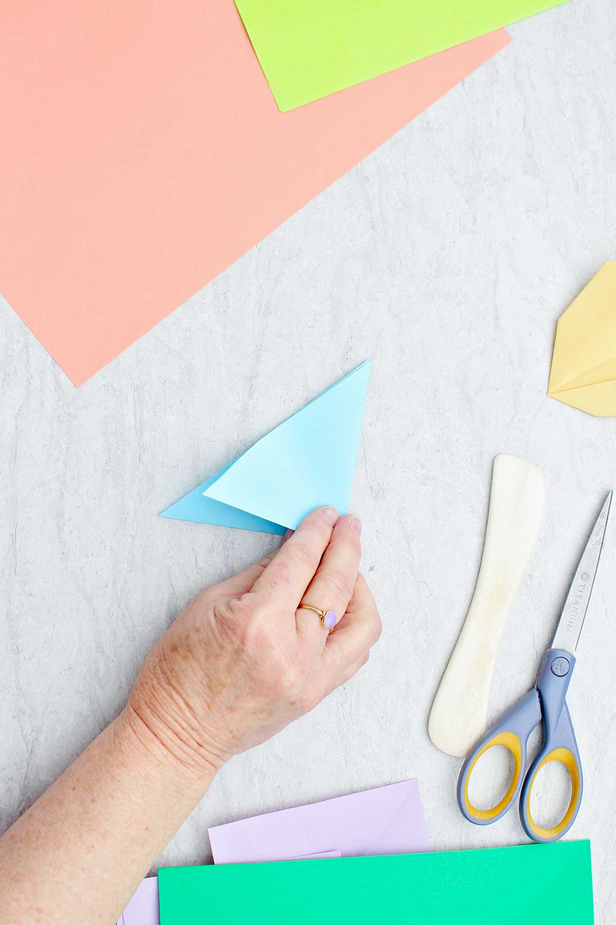 A person folding a light blue piece of paper to make a flower.
