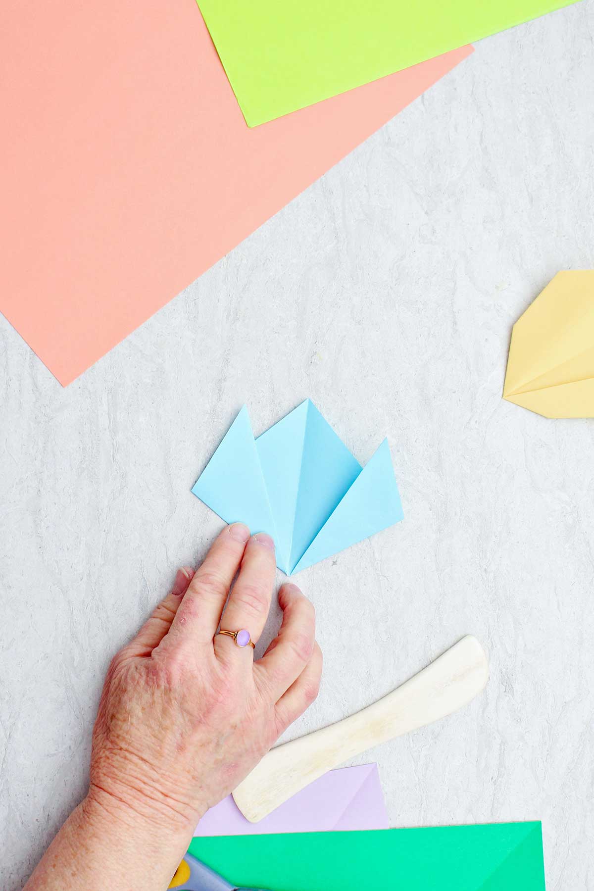 A person folding a light blue piece of paper to make a flower.