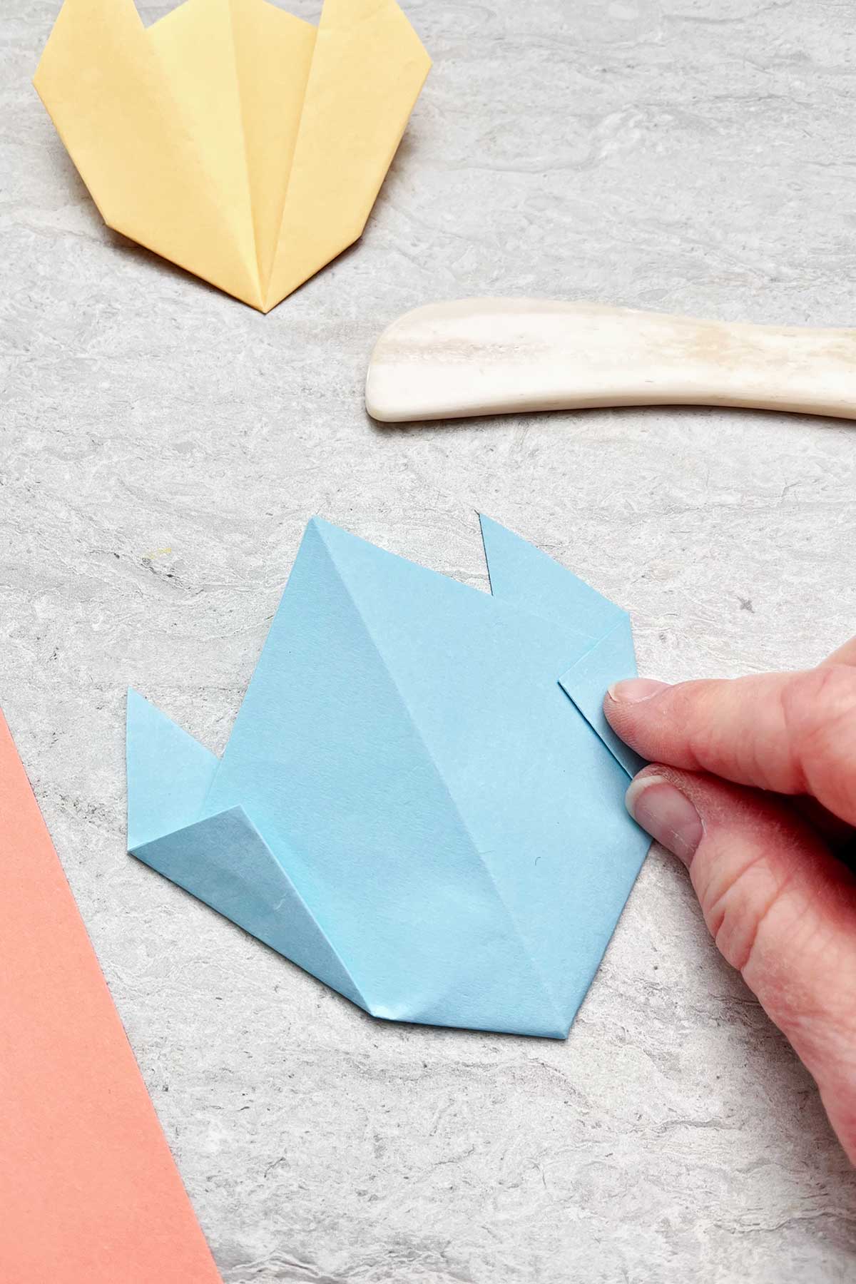 A person folding a light blue piece of paper to make a flower.