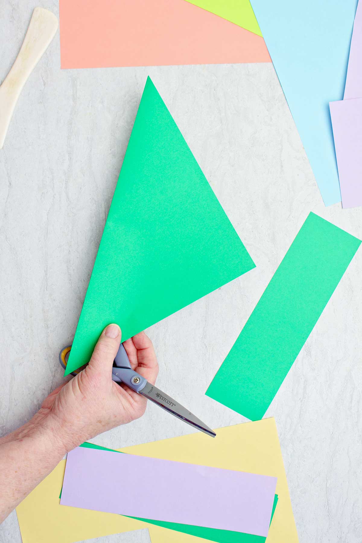 A person cutting a piece of green paper to make an origami flower stem.
