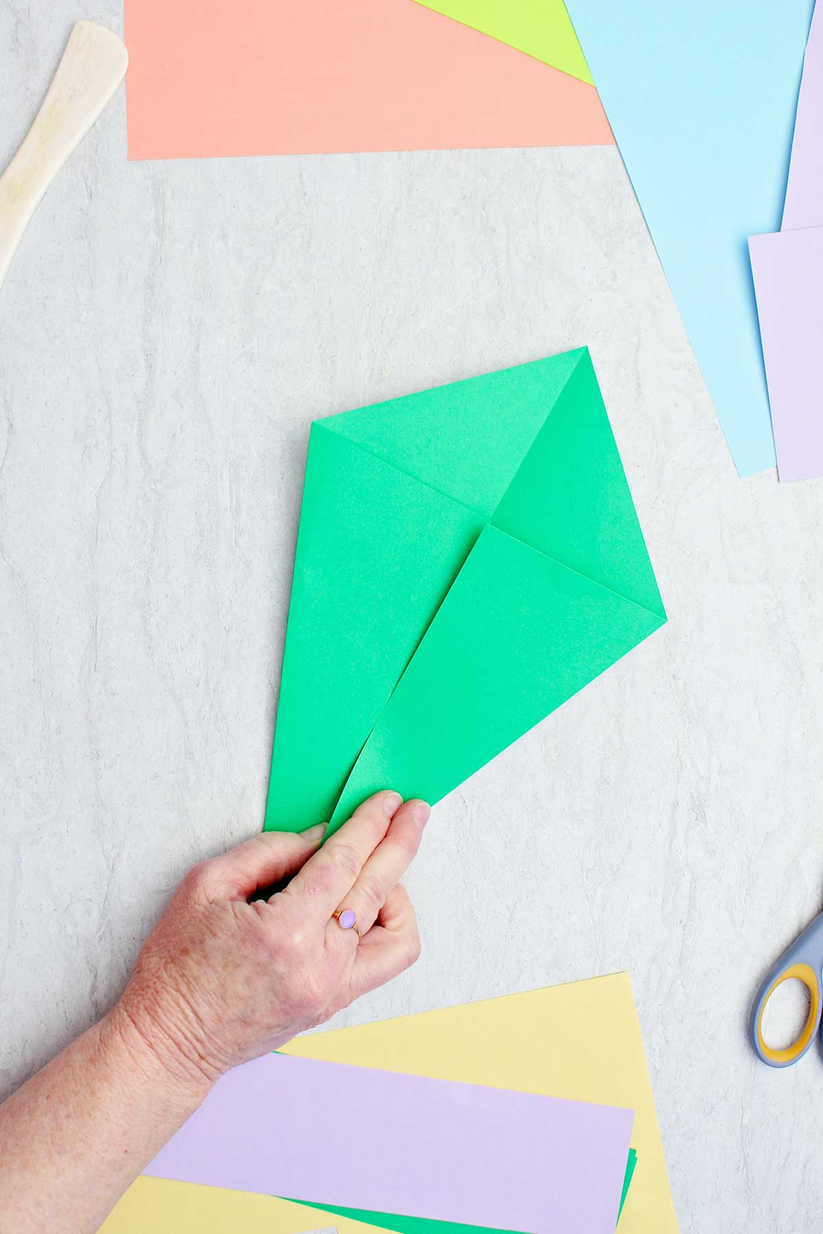 A person folding a green piece of paper to make an origami stem.
