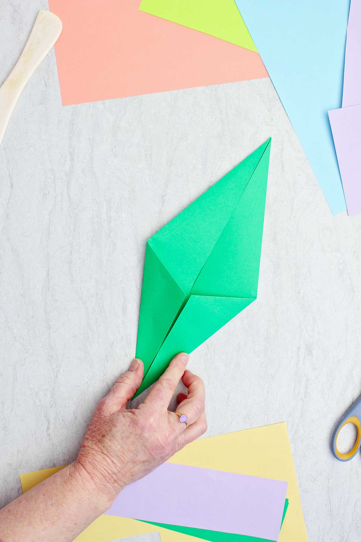 A person folding a green piece of paper to make an origami stem.