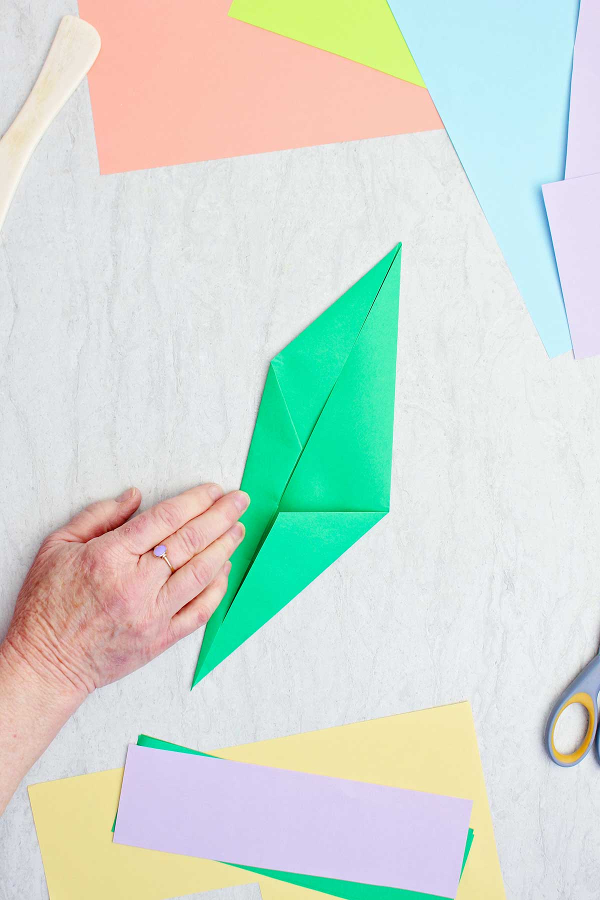 A person folding a green piece of paper to make an origami stem.