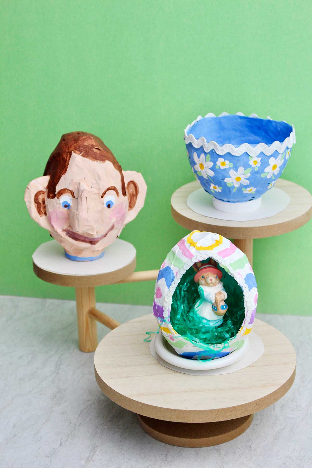 Three different types of paper mache projects on wooden pedestals.