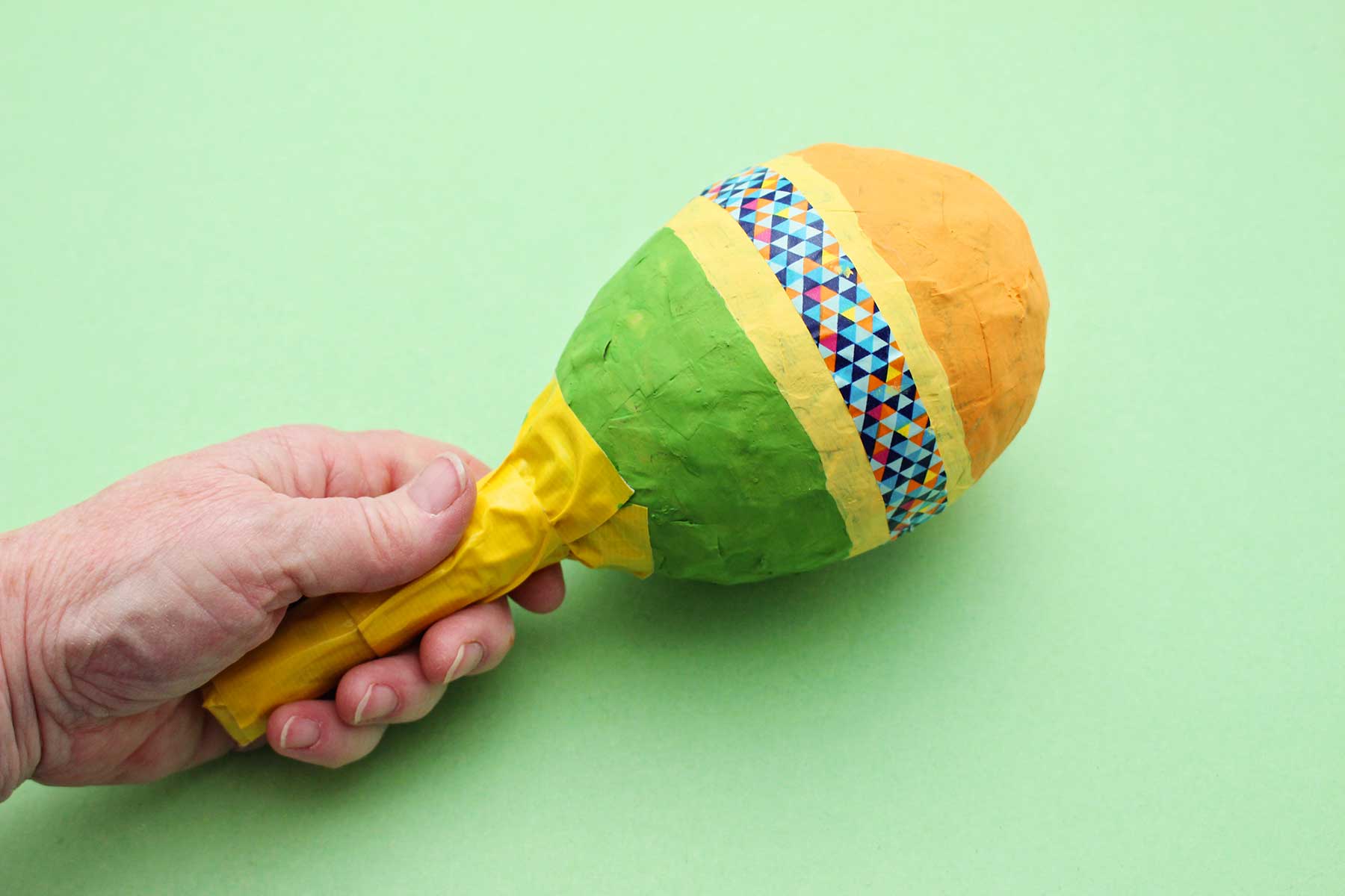 A person holding a paper mache maraca.