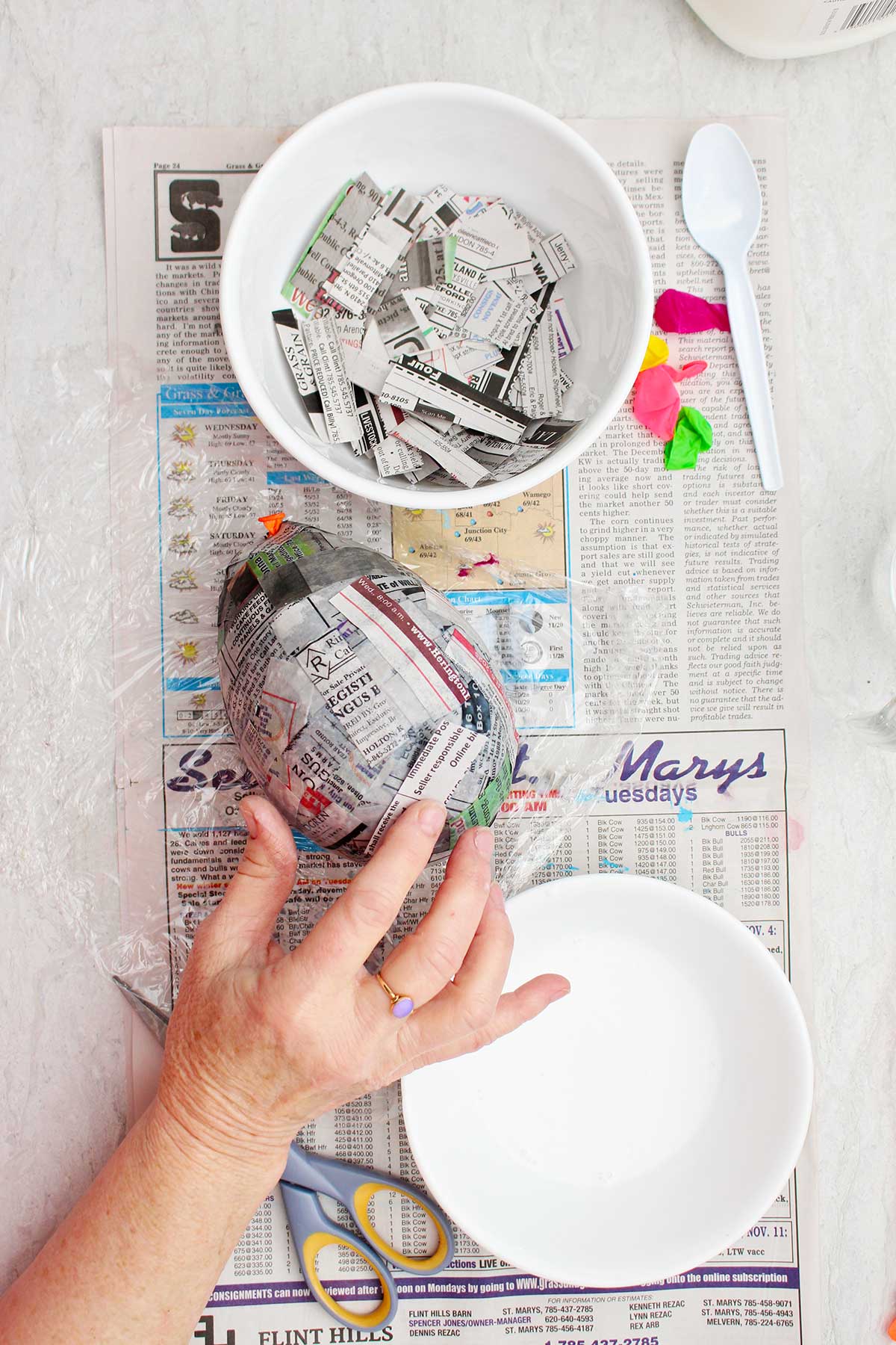 A person pressing paper mache pieces of newsprint to a blown up balloon.