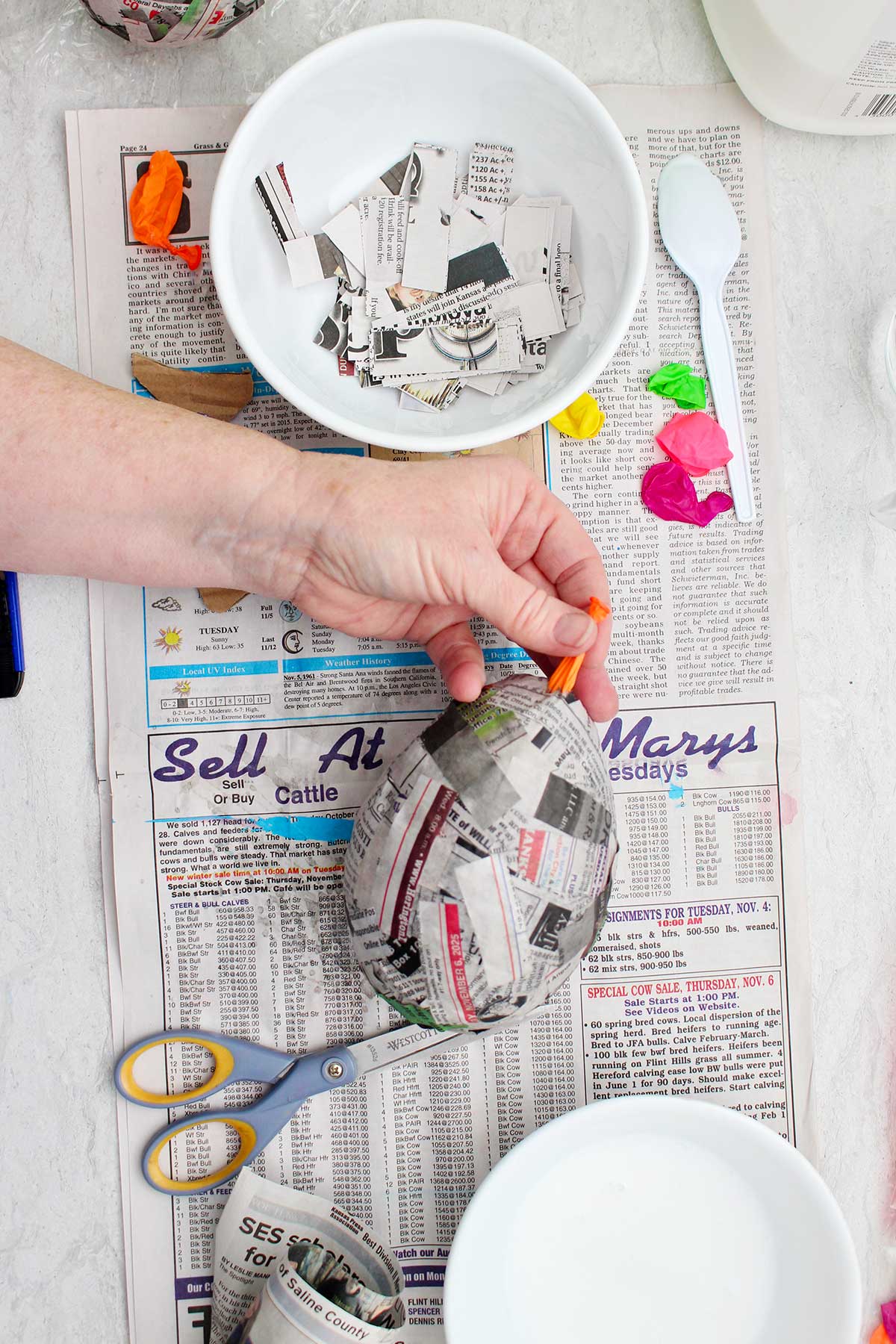 A person pulling out a popped balloon out of a dried paper mache project.